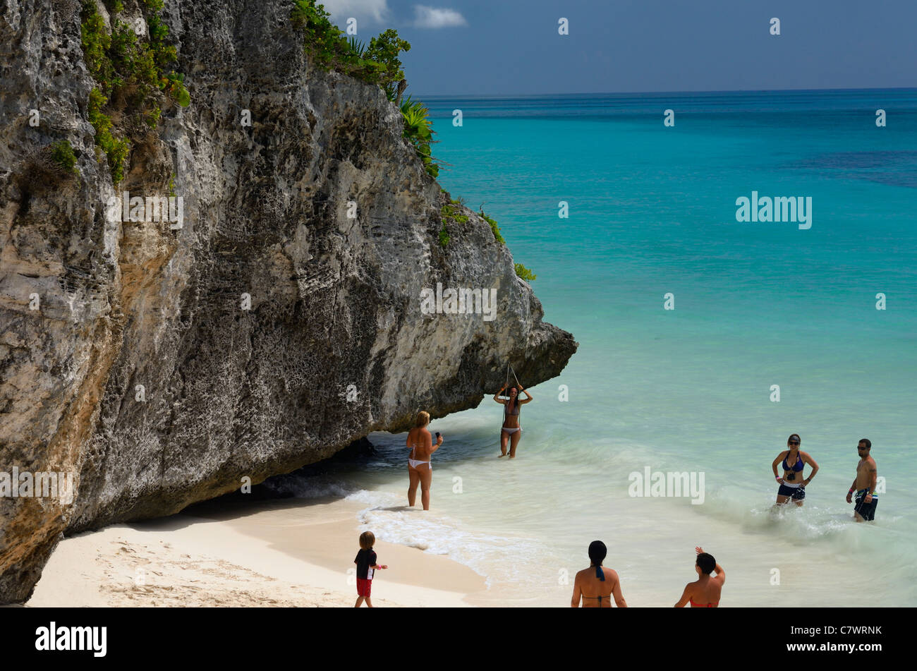 Vacationers playing in the surf of Gulf of Mexico blue Caribbean water by the sea cliffs of