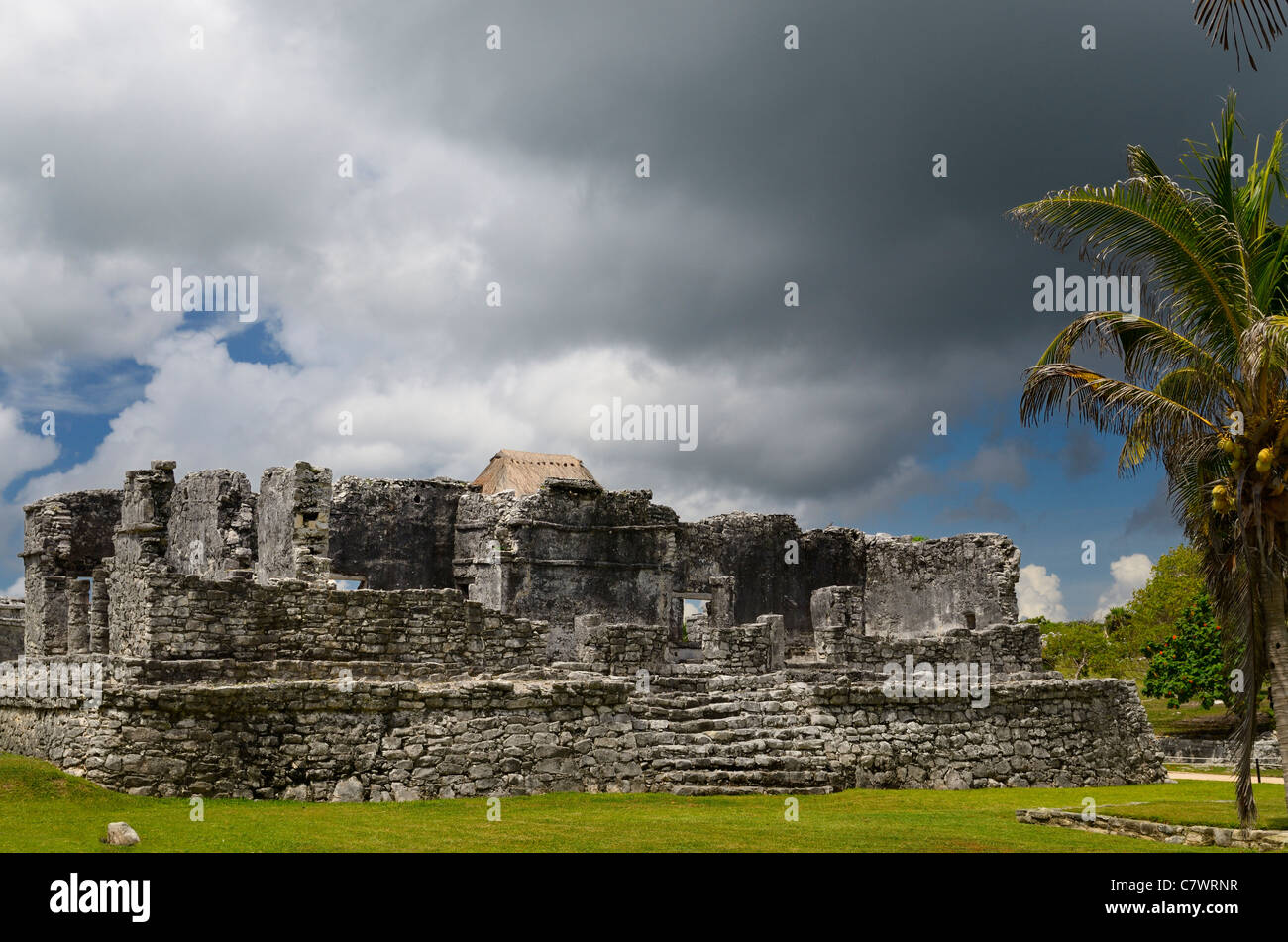 Temple of the Descending God at Tulum Mexico with storm cloud and coconut palm tree Stock Photo