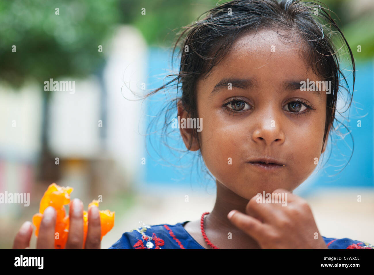 Young poor lower caste Indian street girl holding and eating a traditional indian sweet. Jaangiri / Jangiri / Imarti. Selective focus. Stock Photo