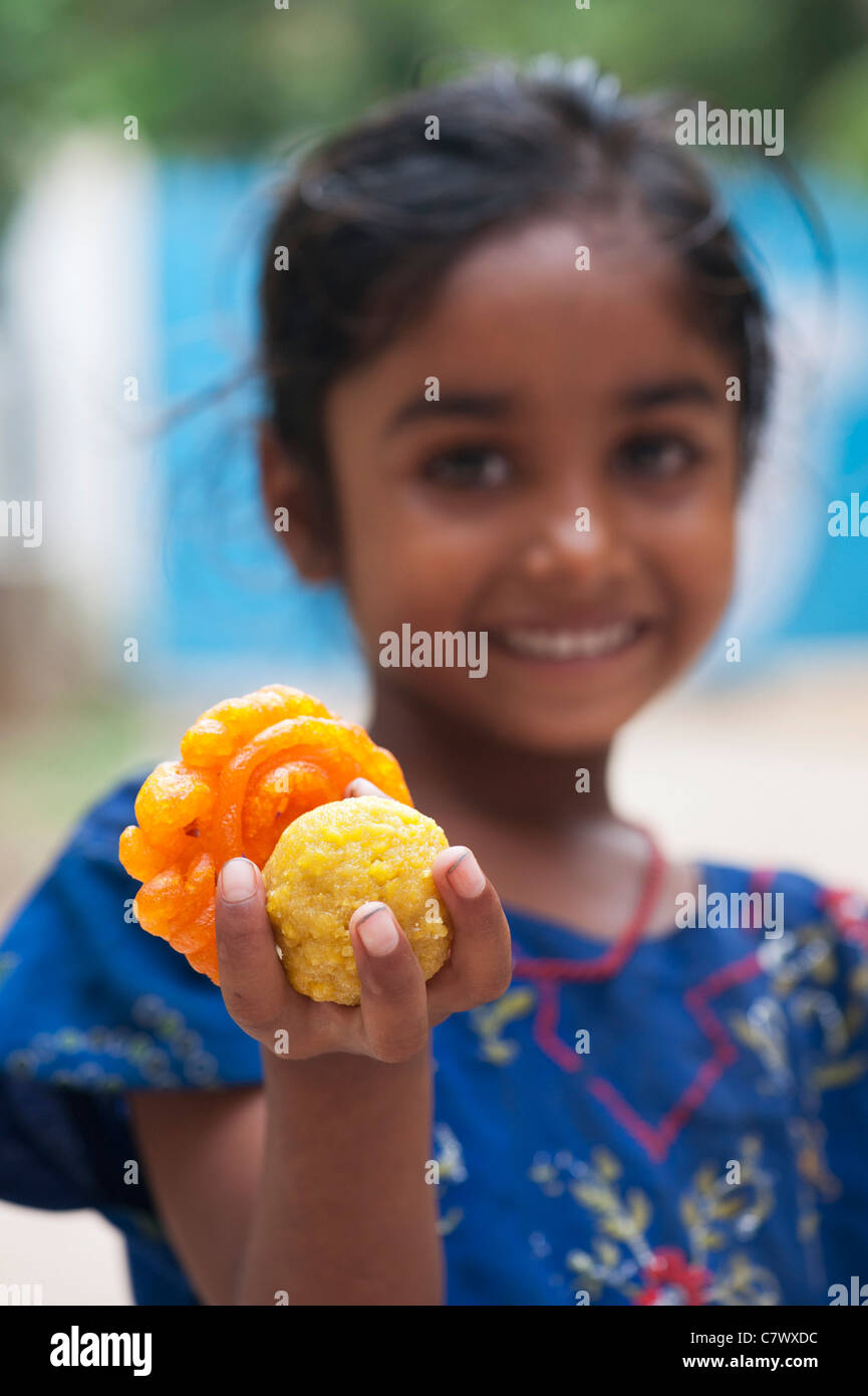 Young poor lower caste Indian street girl holding traditional indian sweets.  Laddu and Jaangiri / Jangiri / Imarti. Selective focus Stock Photo