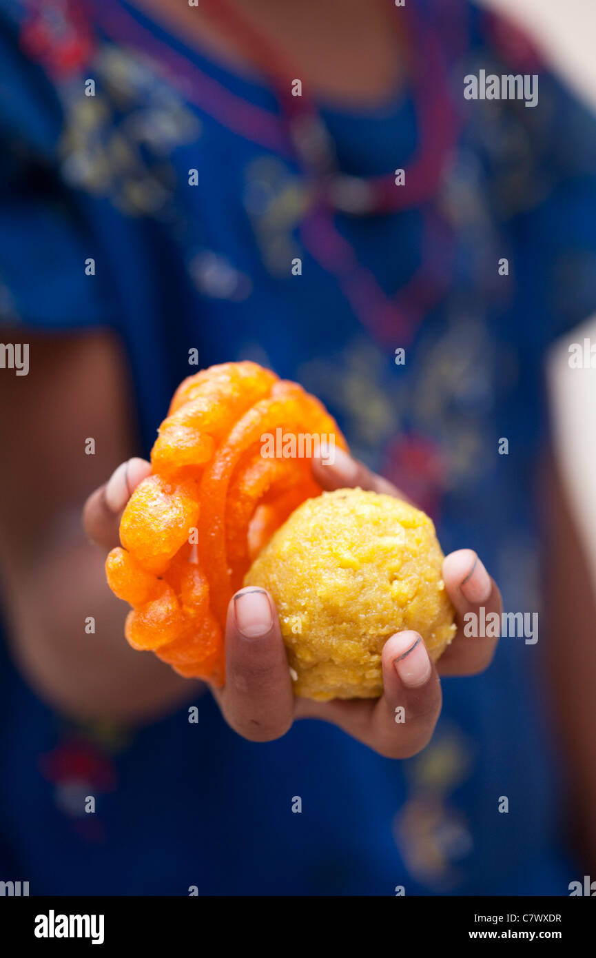 Young poor lower caste Indian street girl holding traditional indian sweets. Laddu and Jaangiri / Jangiri / Imarti Stock Photo