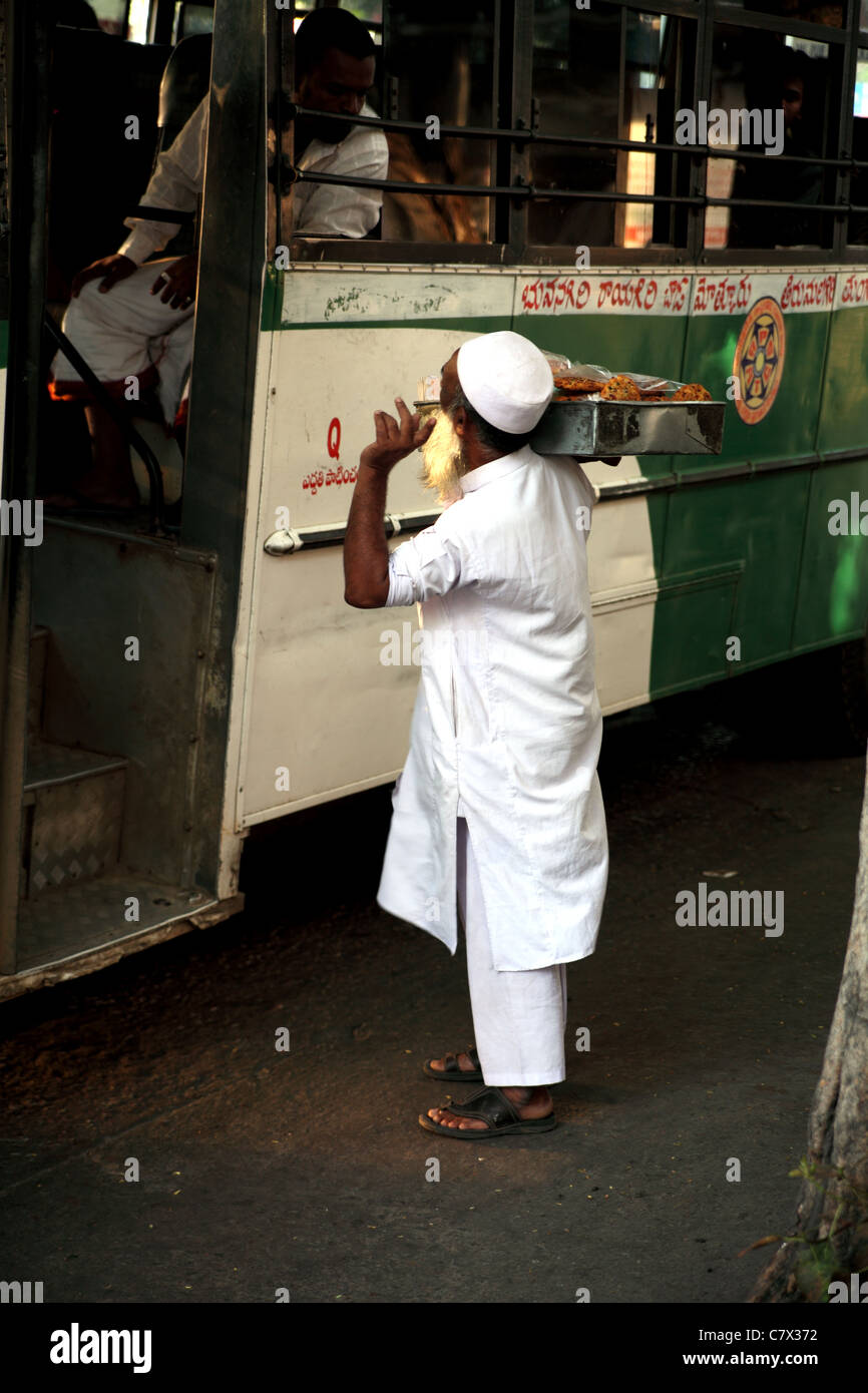 Muslim man in white traditional costume hawks or sells  food to bus passengers in Hyderabad India Stock Photo