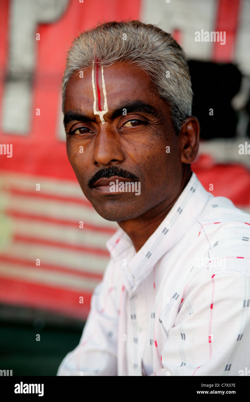 Portrait of Indian man with elaborate making on forehead; in the shape of a trident or trishul, a Hindu symbol; red background Stock Photo