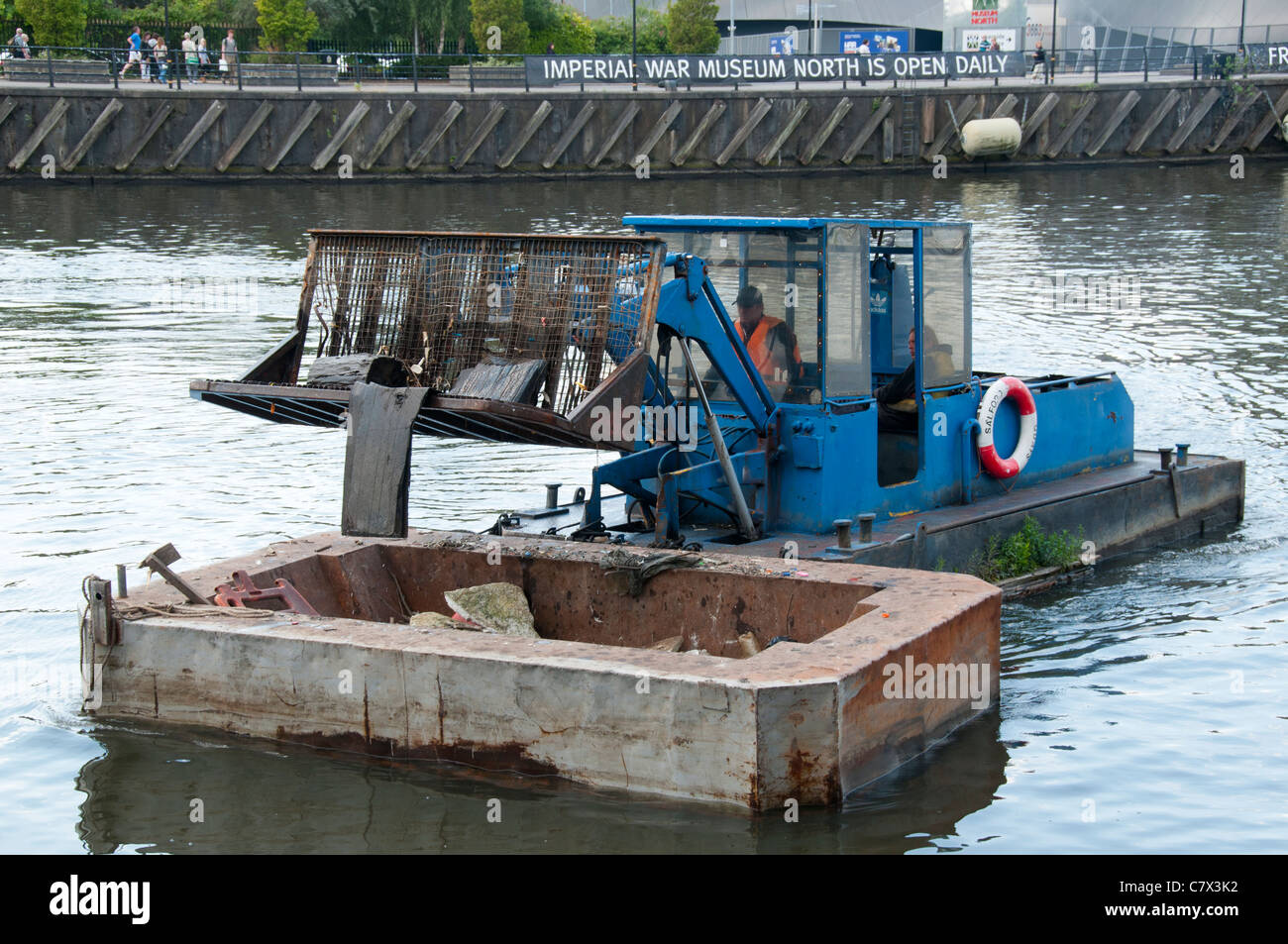 Bucket loader on a barge, clearing floating debris on the Manchester Ship Canal, Salford Quays, Manchester, England, UK Stock Photo