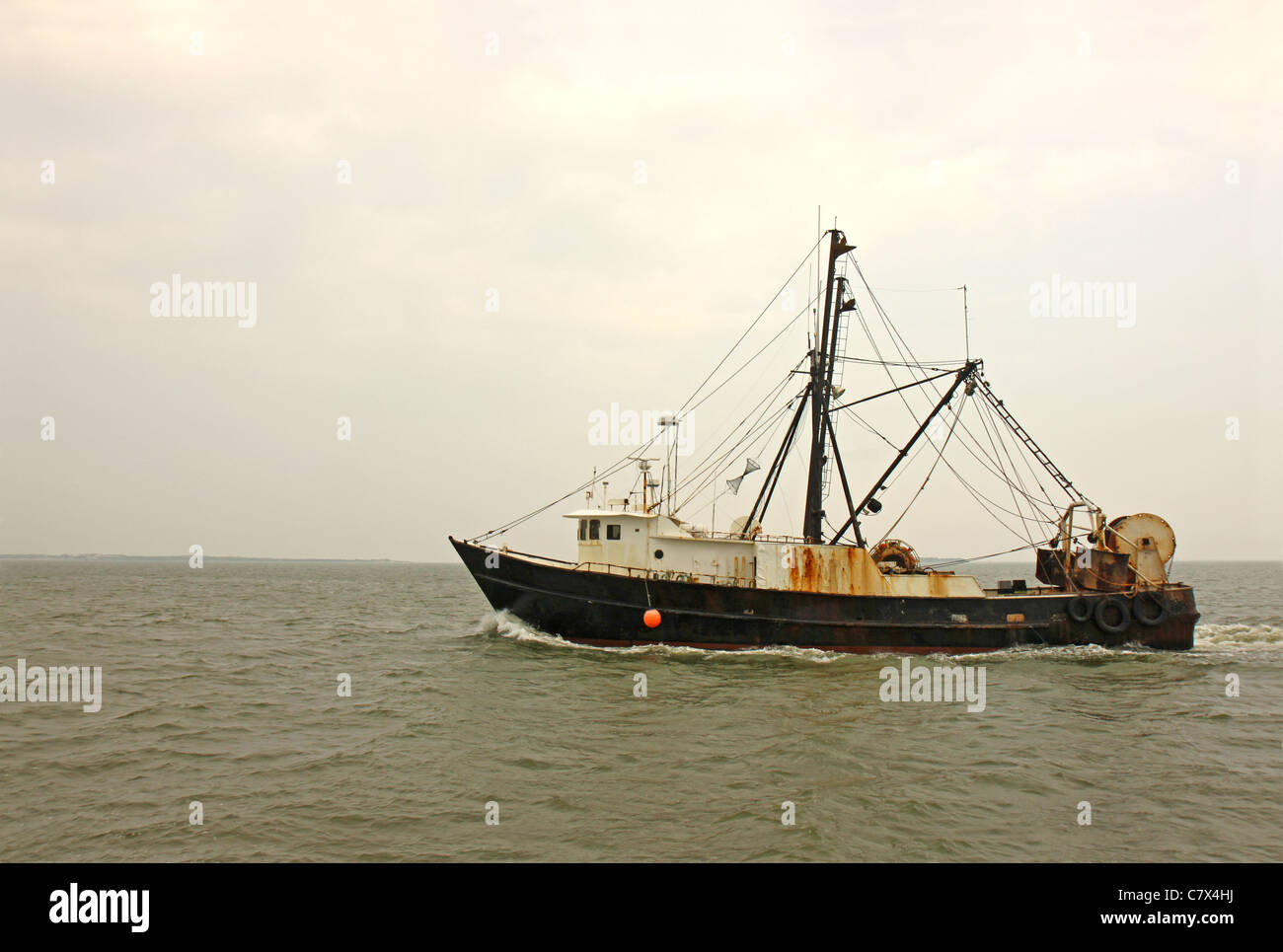 An old, rusty fishing trawler heads for home on Pamlico Sound, North Carolina against the gray mists of an early morning sky Stock Photo