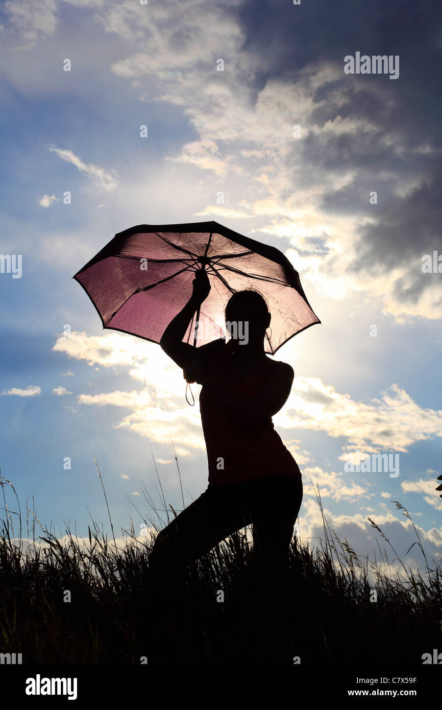 The silhouette of a gymnast stretching with an umbrella in a field ...