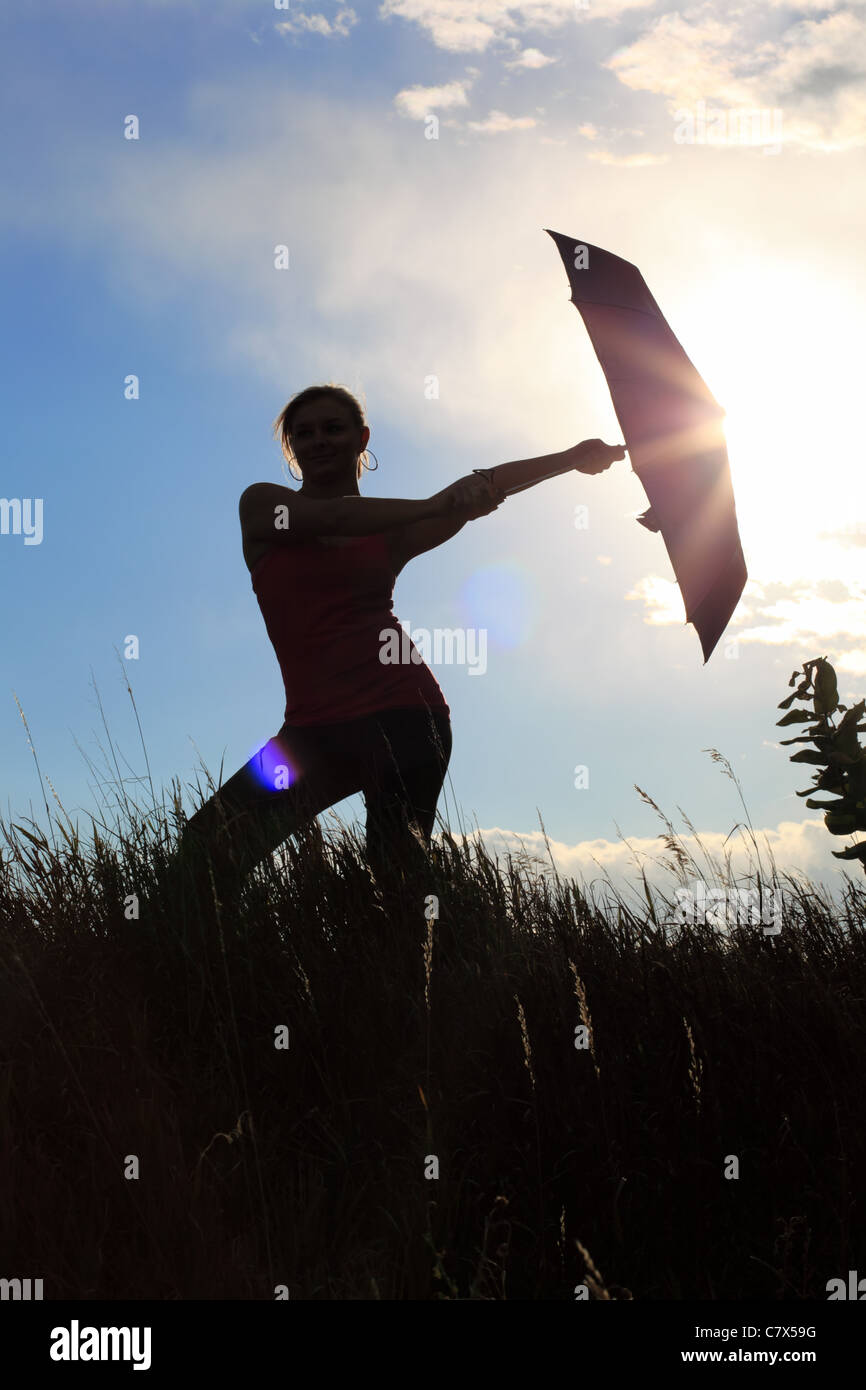 The silhouette of a gymnast stretching with an umbrella in a field ...