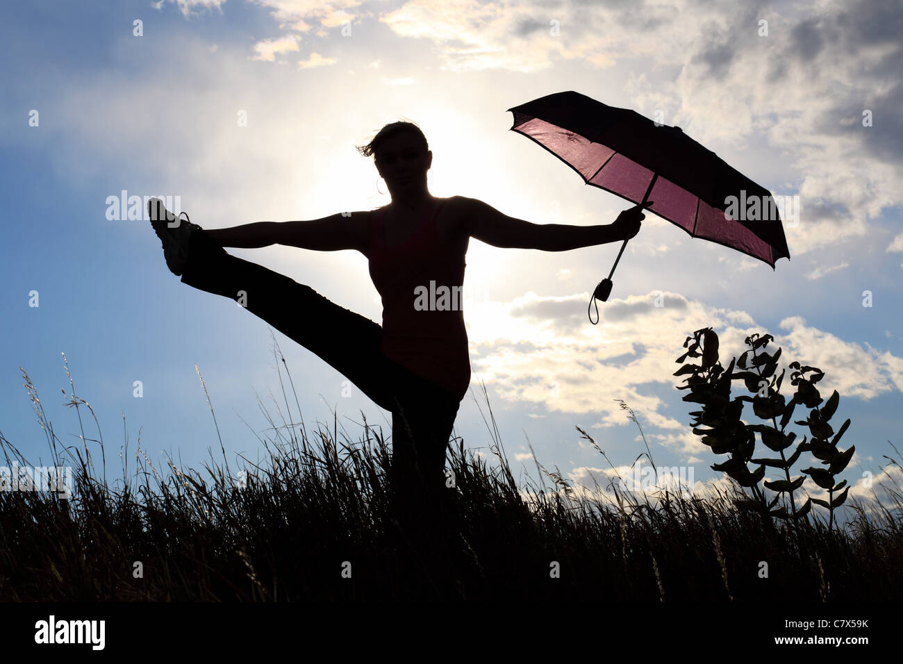 The silhouette of a gymnast stretching with an umbrella in a field ...