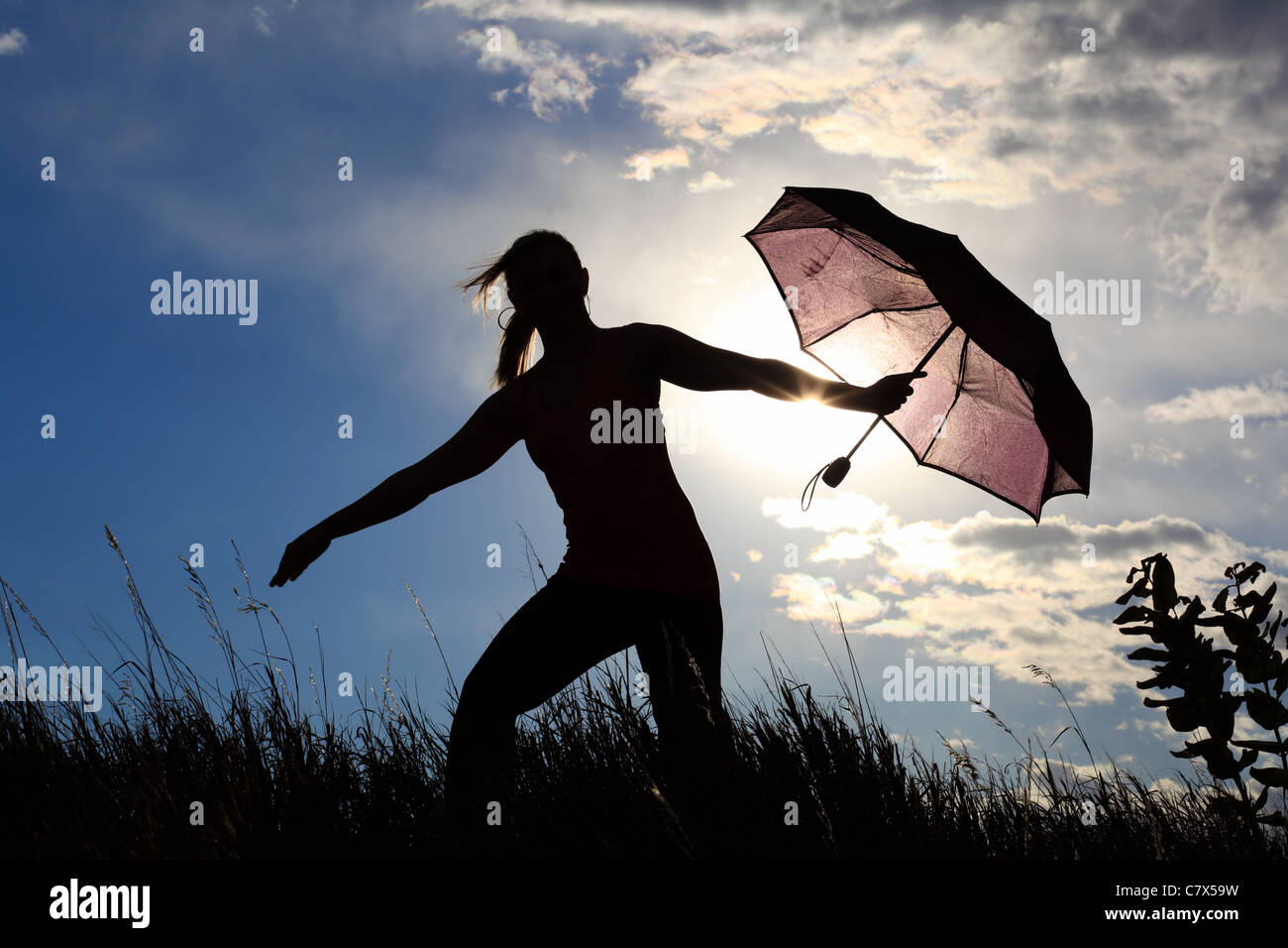 The silhouette of a gymnast stretching with an umbrella in a field ...