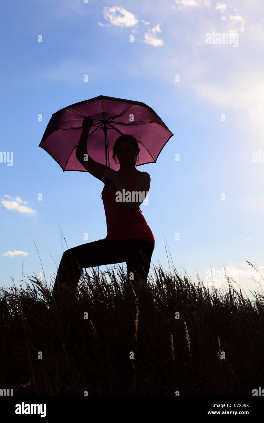The silhouette of a gymnast stretching with an umbrella in a field ...