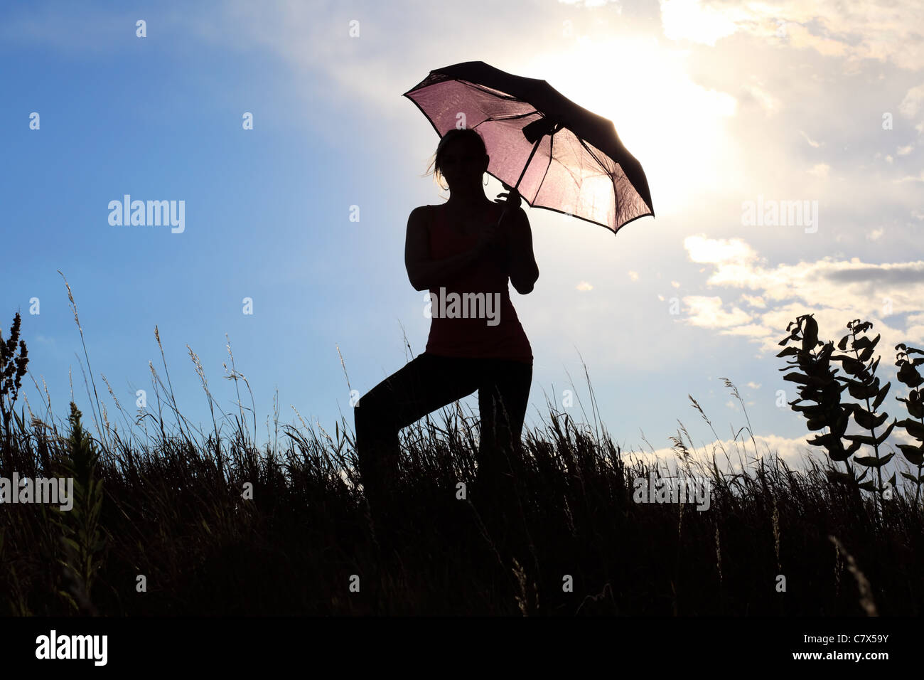 The silhouette of a gymnast stretching with an umbrella in a field ...