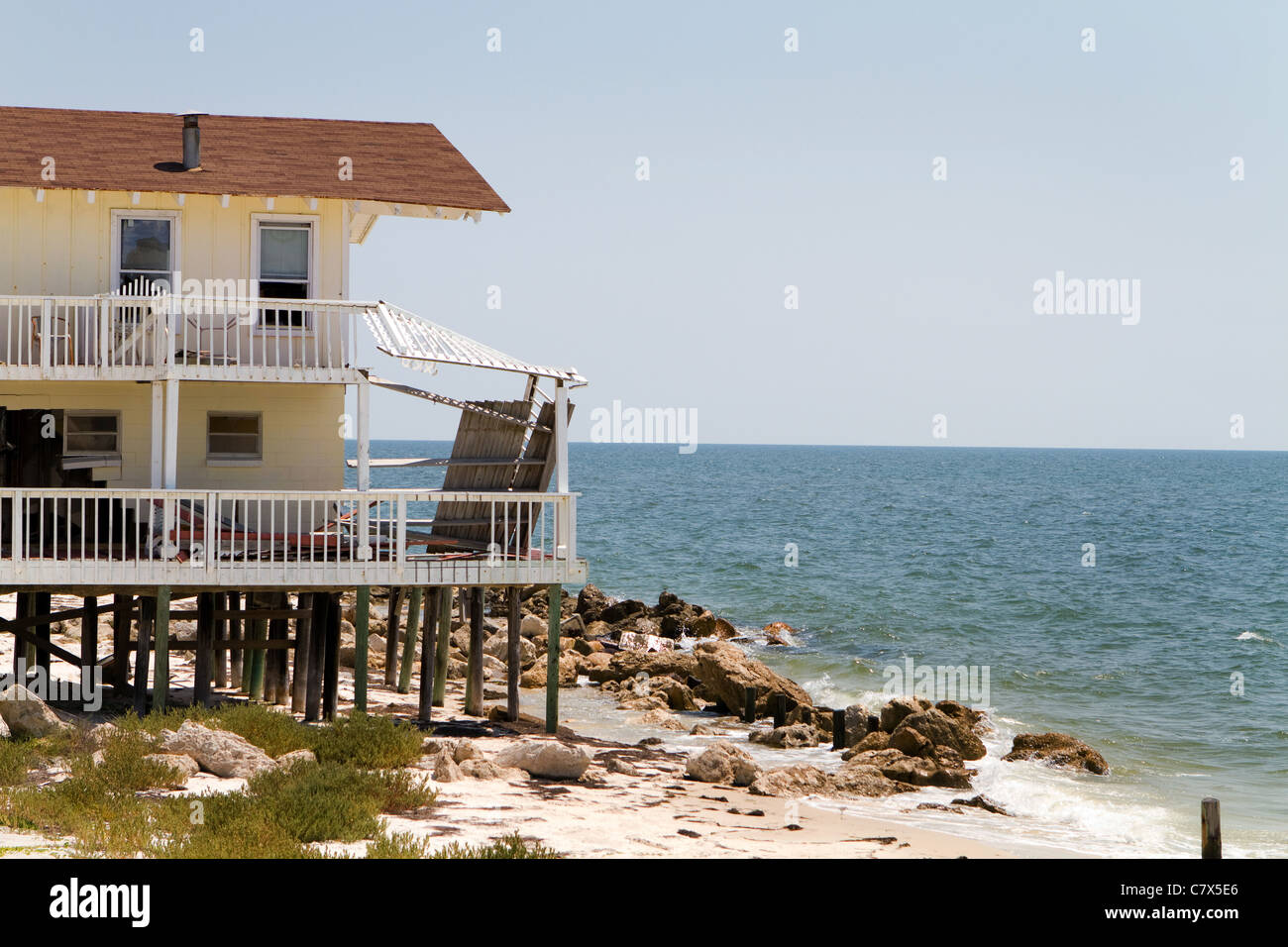 Beach house damaged by wave action and hurricane force winds sits abandoned and vulnerable to the weather. Stock Photo
