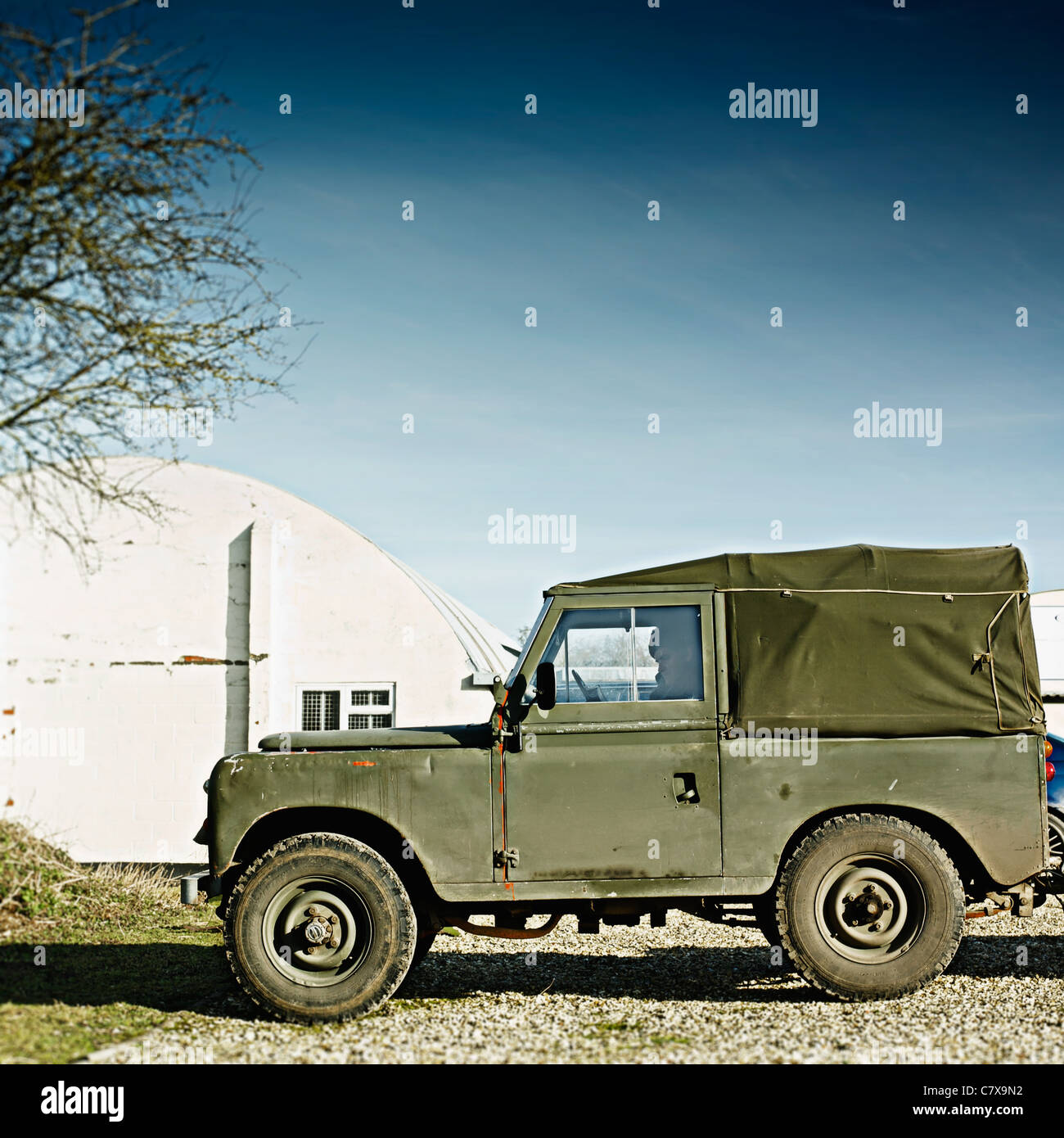 1970's Land Rover Defender Profile shot on a sunny day outside a Nissan hut building. Army green with material roof. Stock Photo