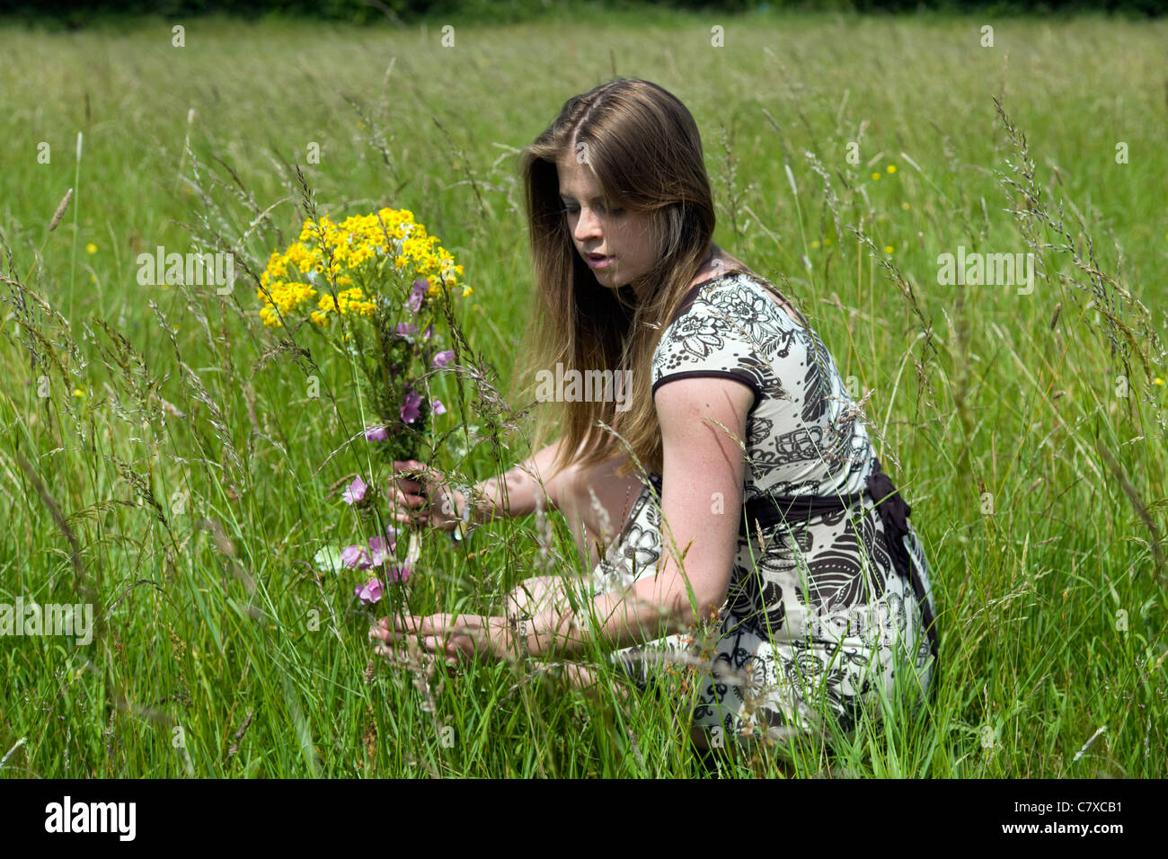 Attractive young caucasian woman picking wildflowers in meadow on