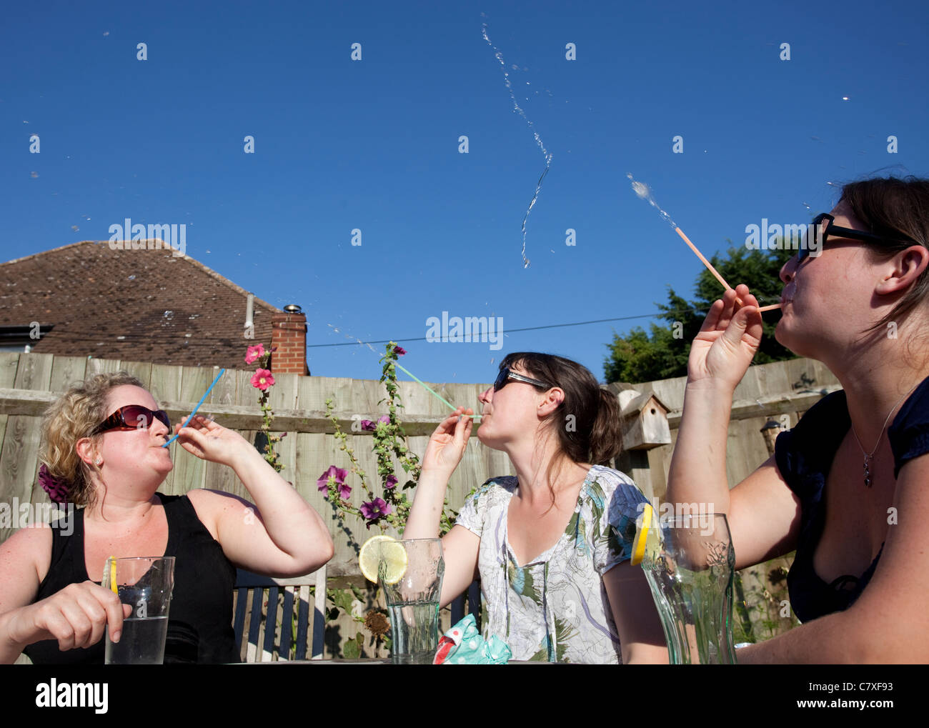 three women spraying water through straws at each other Stock Photo Alamy