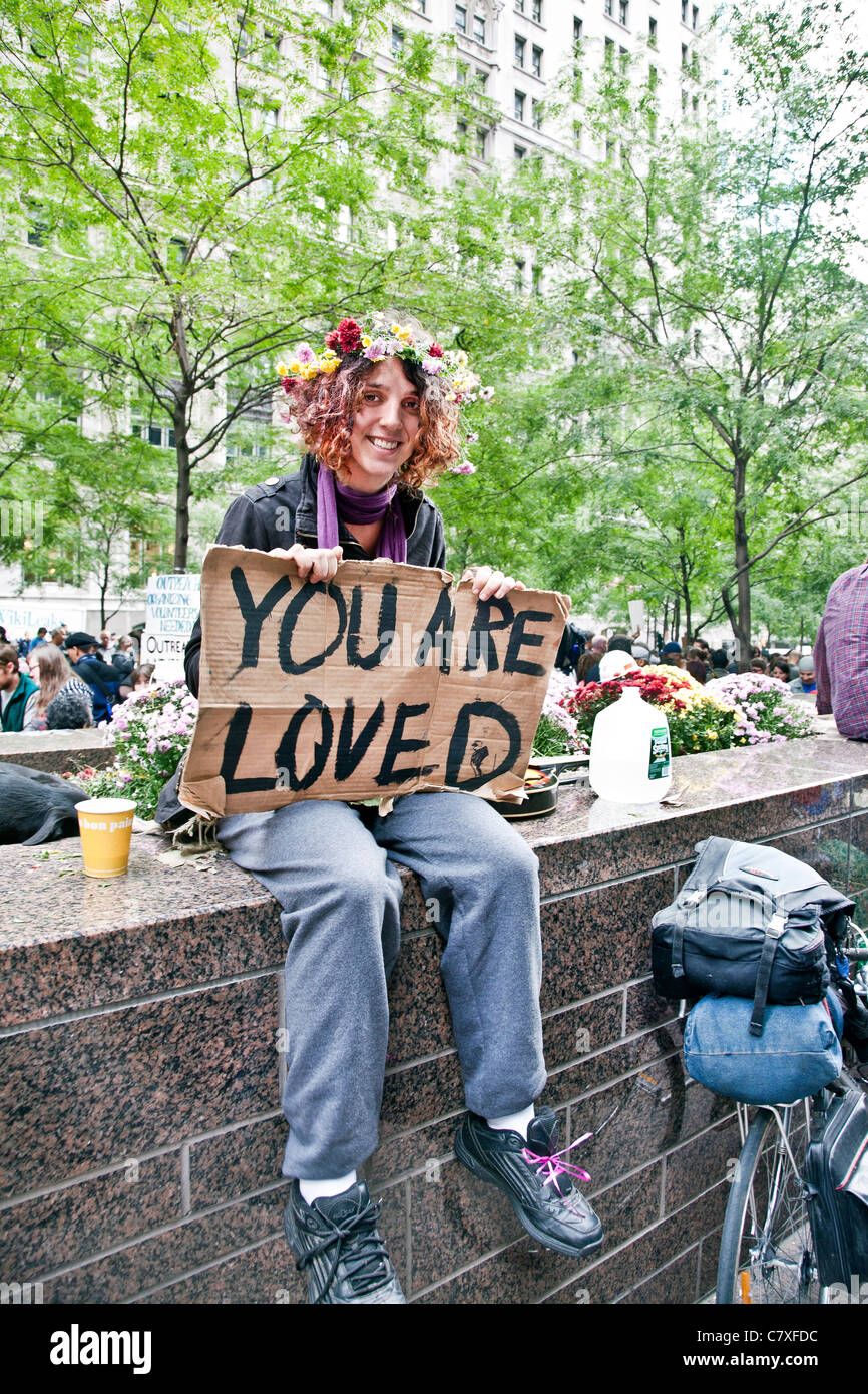 pretty young occupy Wall Street protestor sitting on wal at Zuchotti Square holds a card board sign indicating peace & community Stock Photo