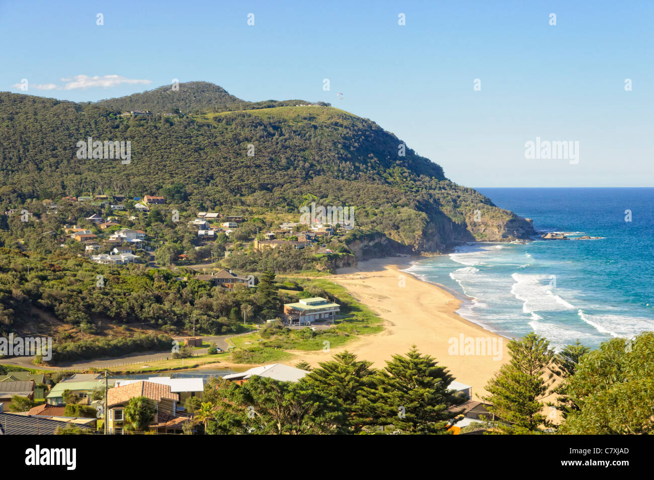 Small town next to an idyllic rural surf beach in a sheltered bay between forested hills. Stock Photo