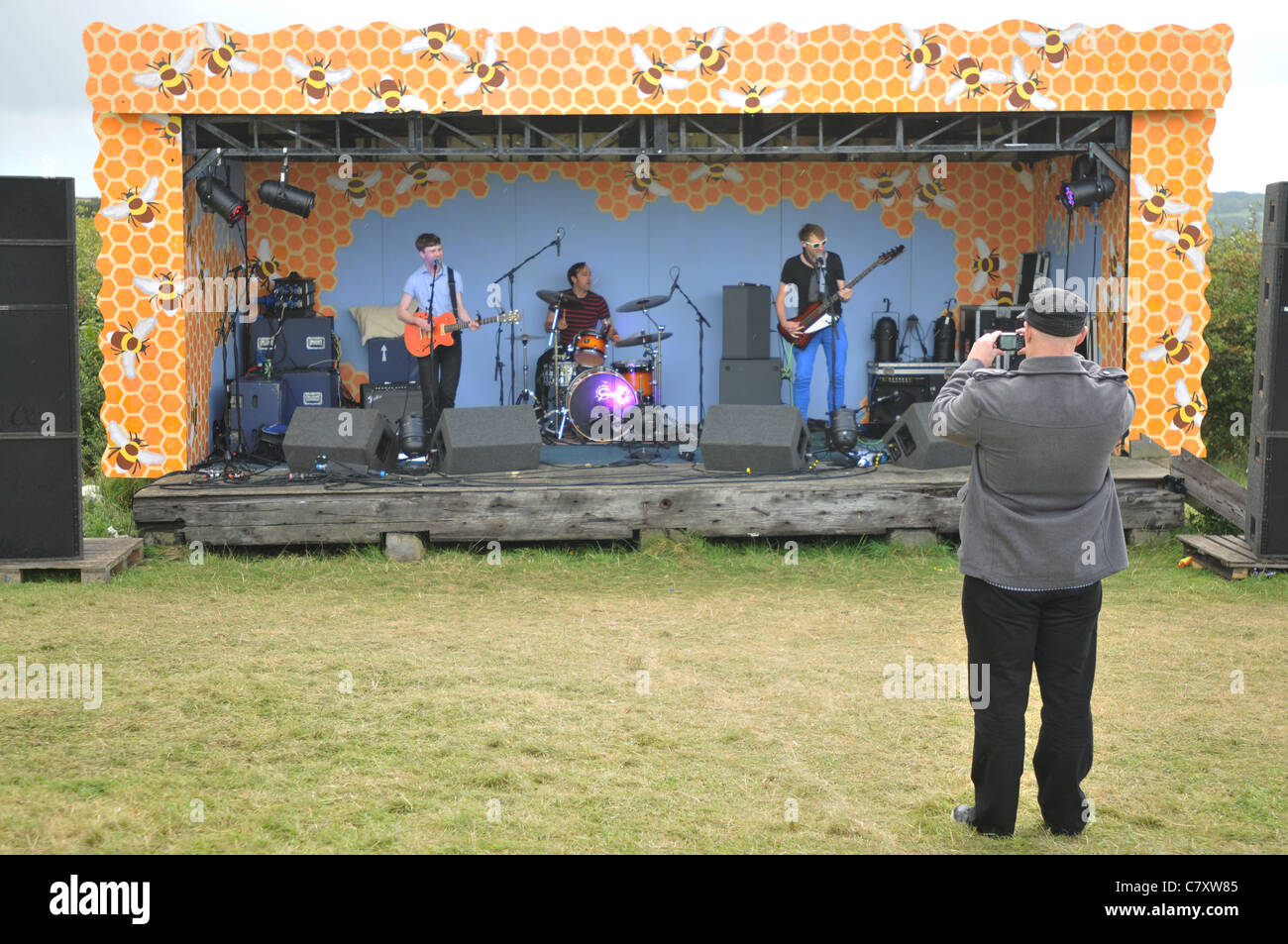 A n old man photographs a band at Holifield festival in Gweek, Cornwall playing to an empty field. Stock Photo
