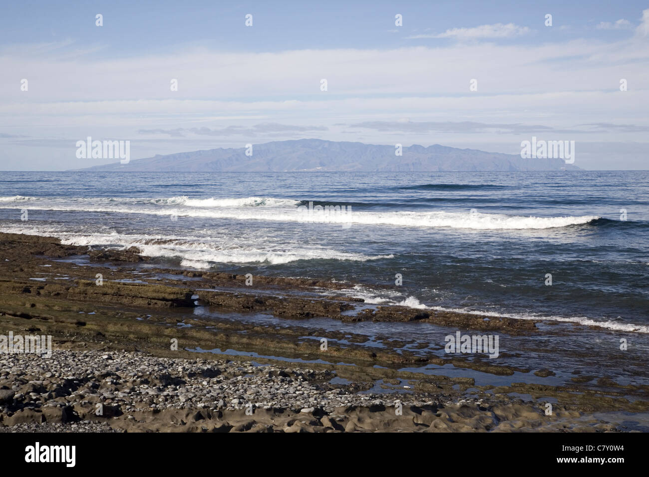 Layered rocks on the beach of Playa de las Americas with the island La Gomera in the background, Canary Islands, Spain Stock Photo