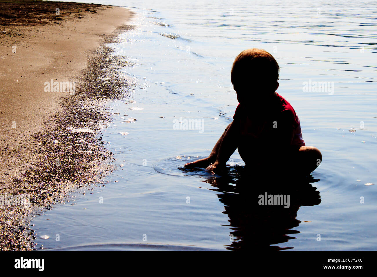 Silhouetted baby playing in shallow water at beach Stock Photo