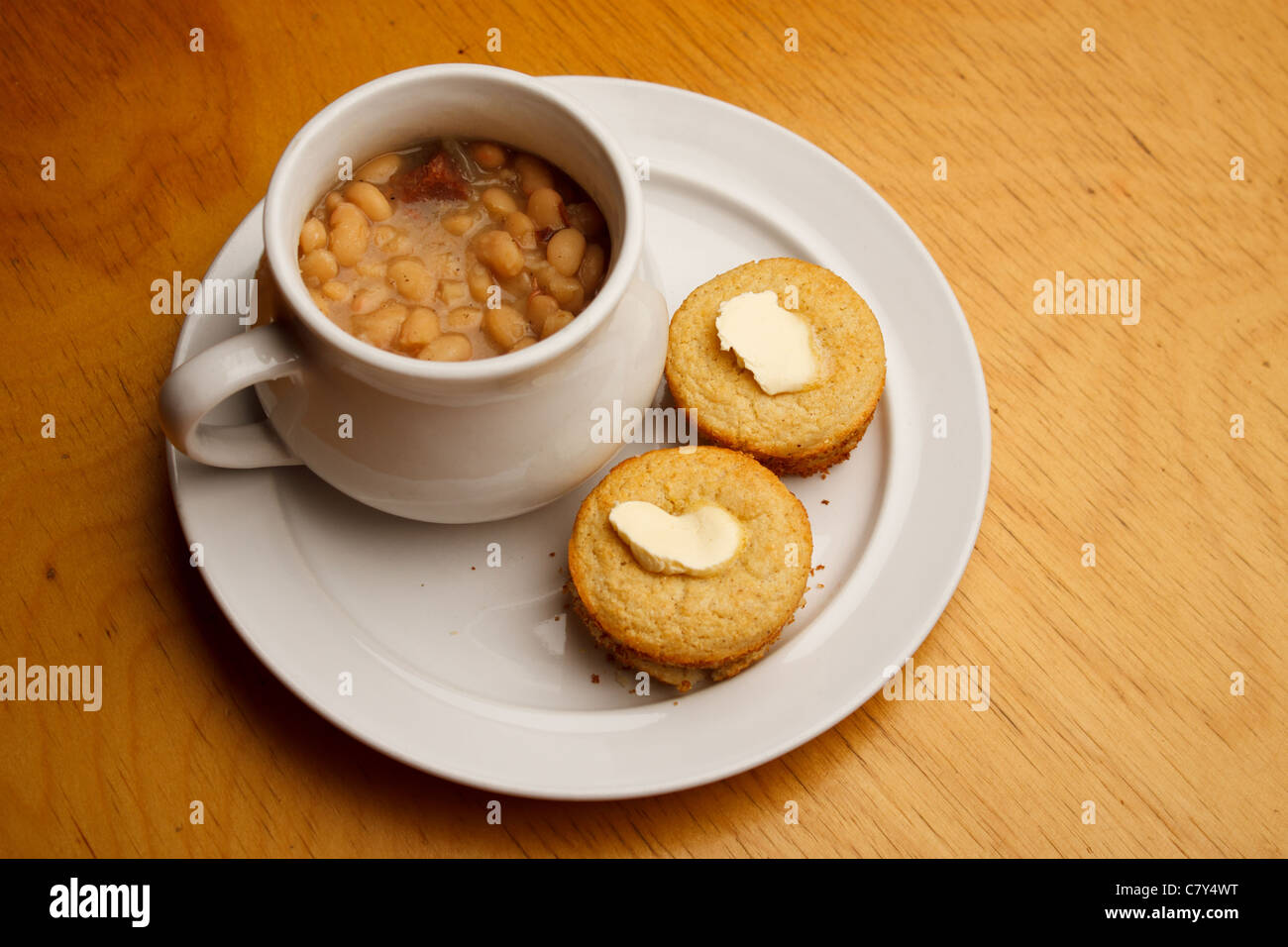 Cupcake style buttered cornbread on a white plate with bowl of bean soup Stock Photo
