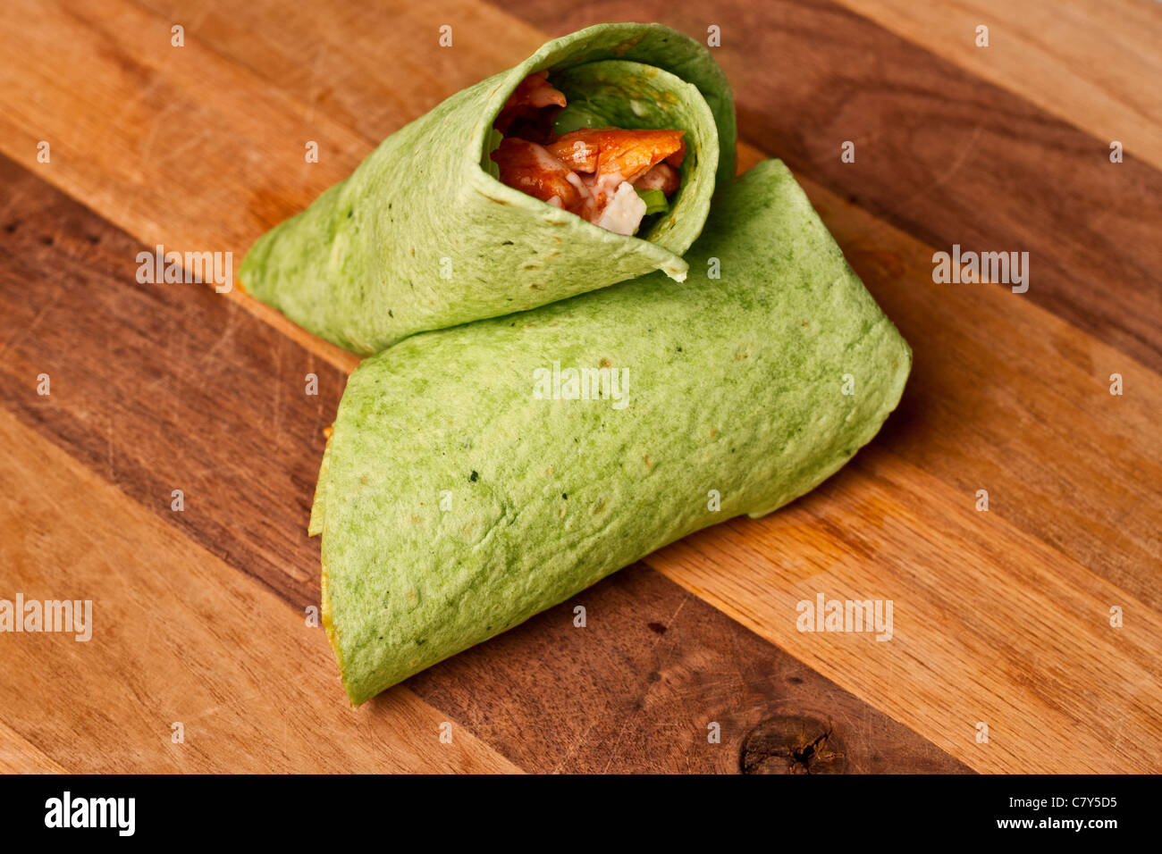 Buffalo chicken wrap in spinach tortilla on wooden surface Stock Photo