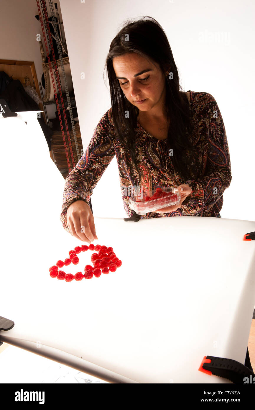 A young woman assistant setting up a photo shoot of fresh raspberries ...