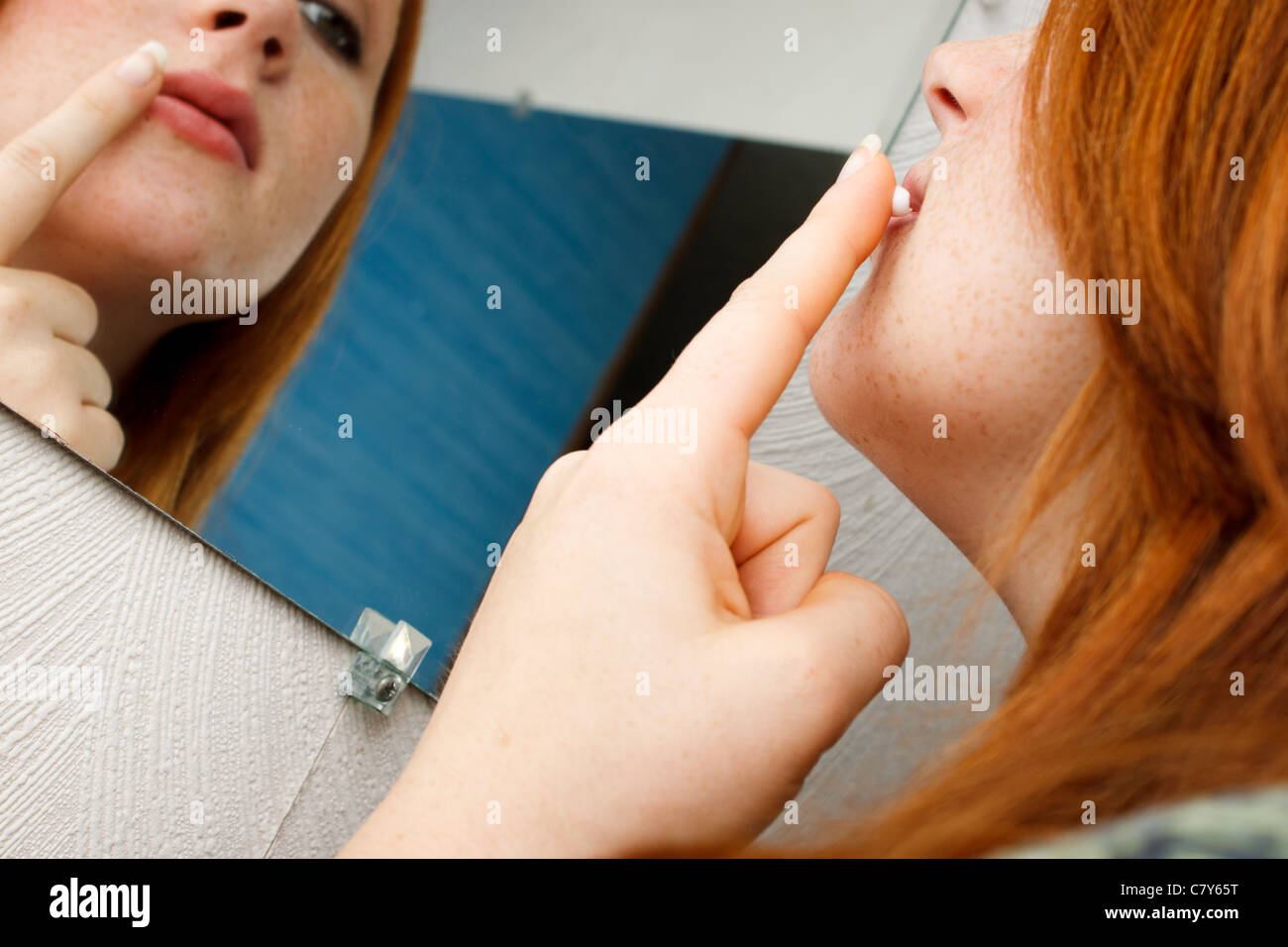 Red head girl applying white cream to her lip in a mirror Stock Photo
