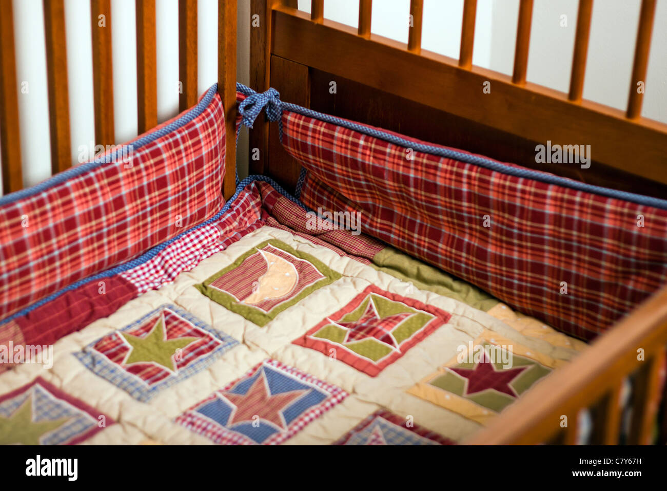 Comforter and bumper in empty baby crib Stock Photo Alamy