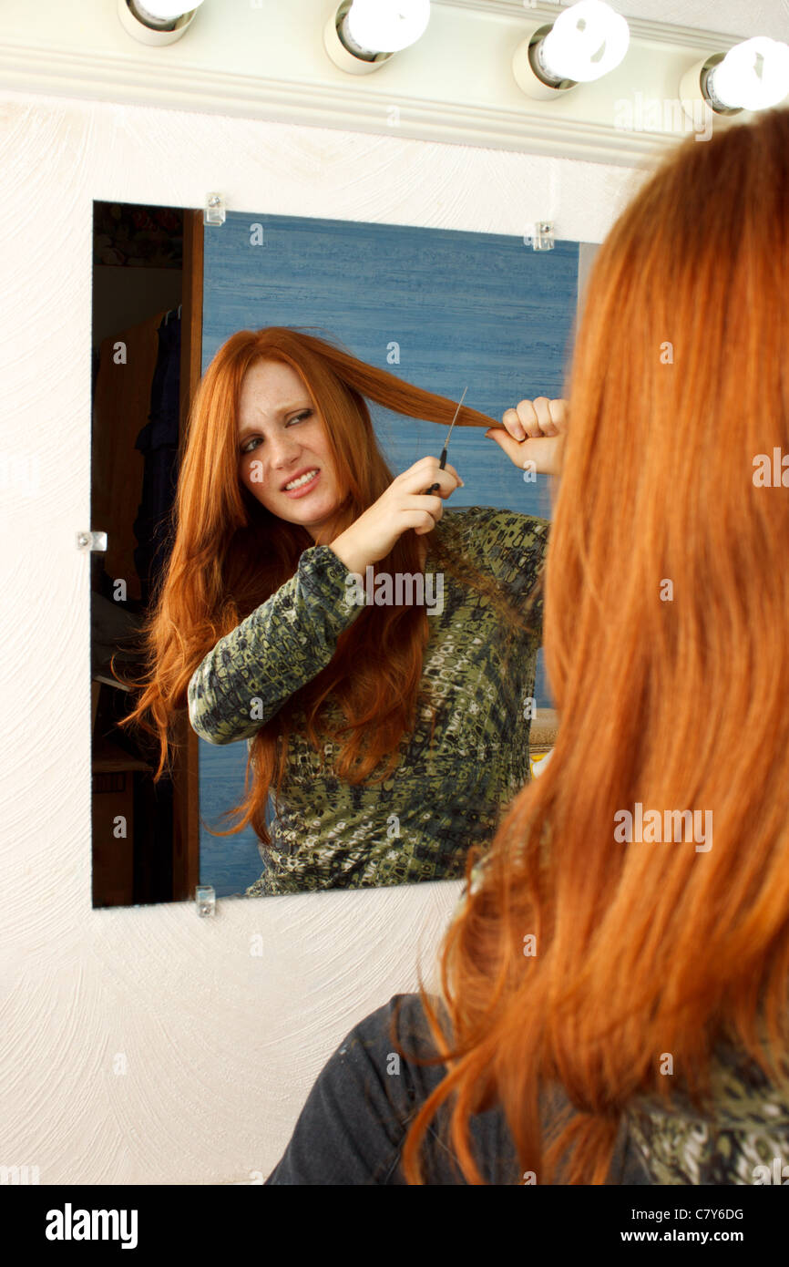 Beautiful red head woman uneasy about cutting her own hair Stock Photo