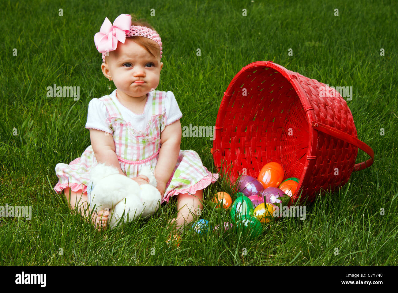 Baby girl frowning beside a spilled Easter egg basket Stock Photo