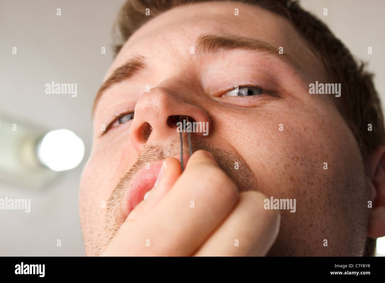 Man pucking nose hair with tweezers while facing camera Stock Photo