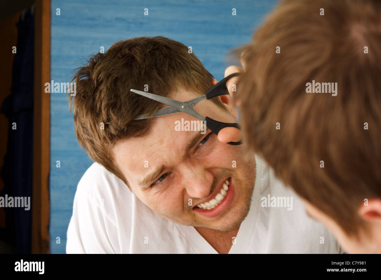 Young man preparing in mirror to cut hair himself with nervous expression Stock Photo
