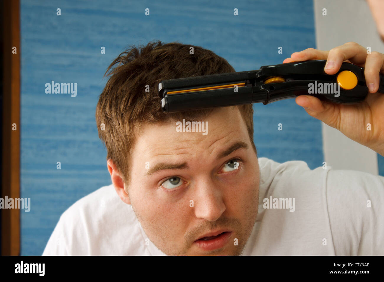 Young man attempting to straighten bangs in mirror with straightener Stock Photo