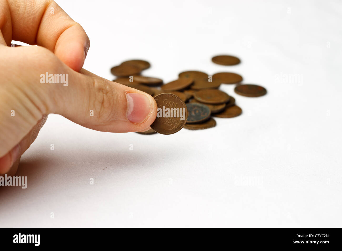 Person pinching a wheat penny in front of a small pile of wheat pennies on a white background Stock Photo