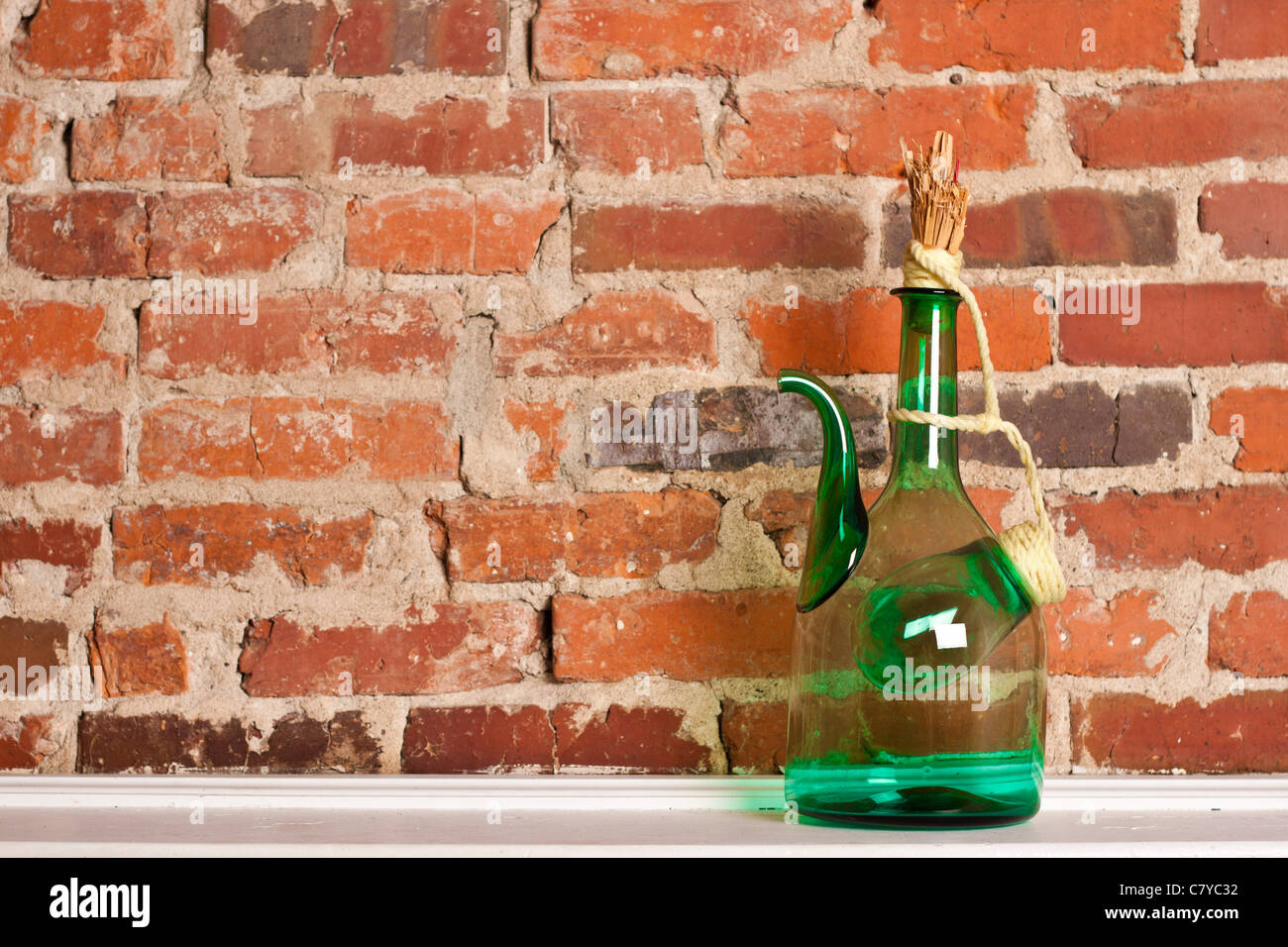 Green glass wine jug on white surface against brick wall Stock Photo