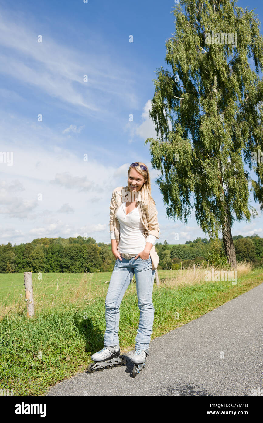Inline skating young woman wearing jeans on sunny asphalt road Stock
