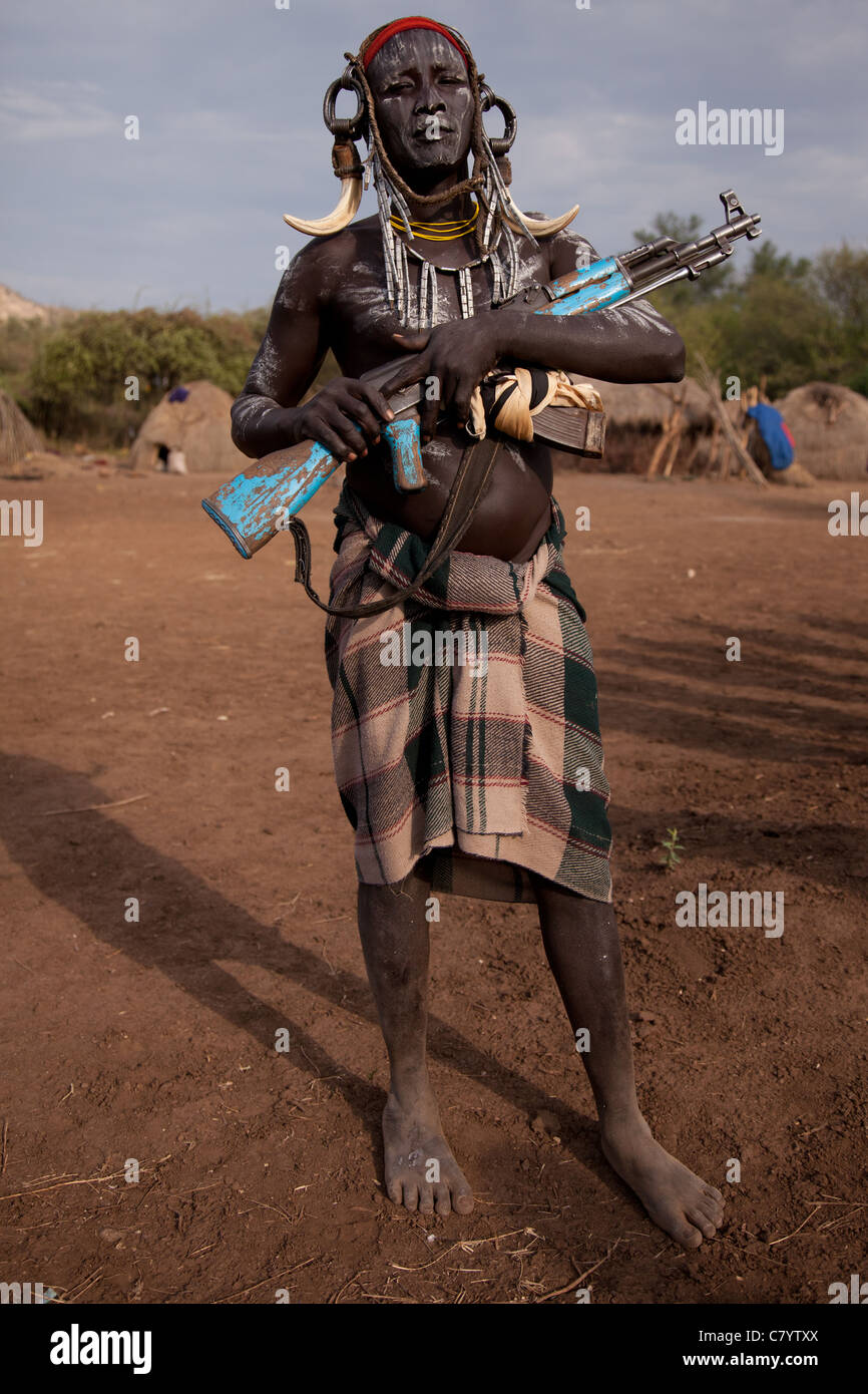 Mursi warrior standing in traditional dress with AK47 guns,  Jinka, Omo Valley, Ethiopia, Africa Stock Photo