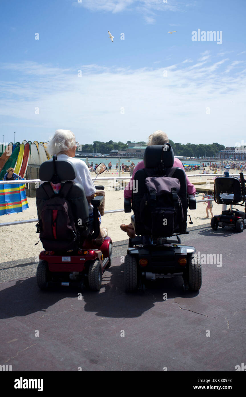 Two ladies in mobility scooter on the promenade of Weymouth beach, Devon Stock Photo