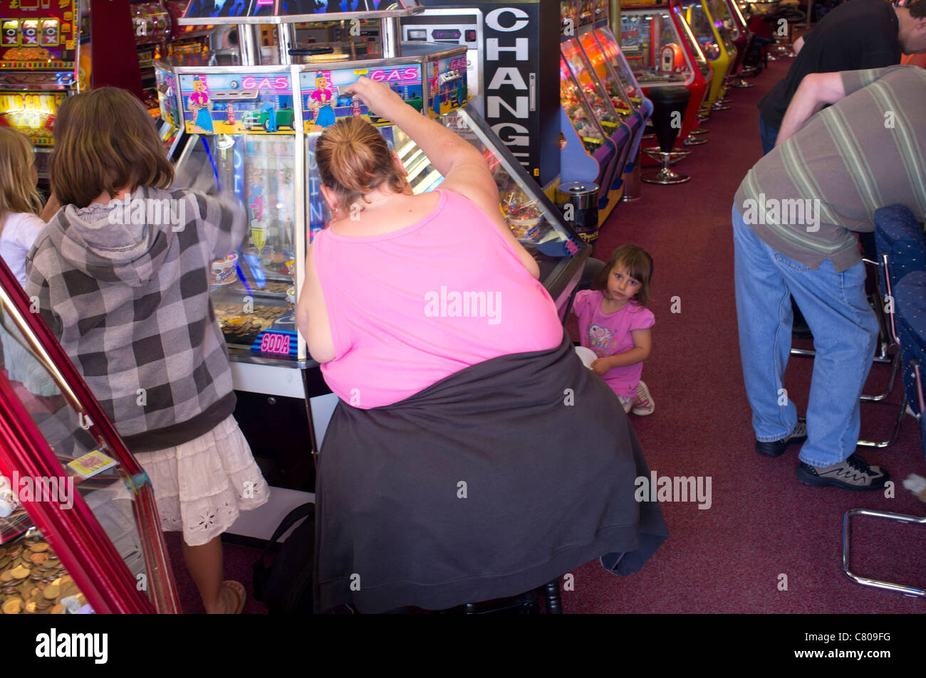 A woman surrounded by children playing in an amusement arcade, Weymouth, Dorset, UK Stock Photo