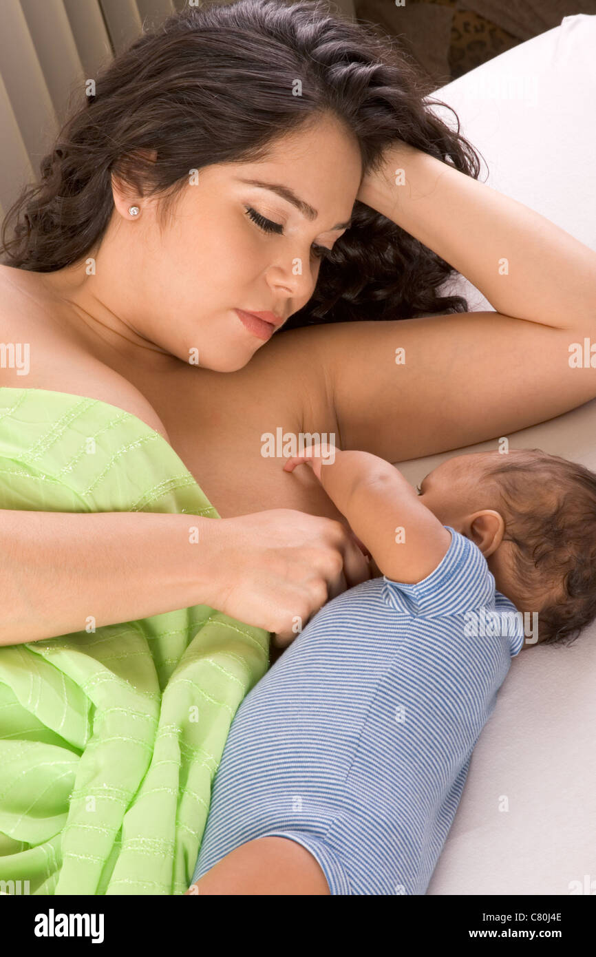 Latina woman lying on bed and breastfeeding her 2 months old baby of mixed Hispanic and African-American ethnicity Stock Photo