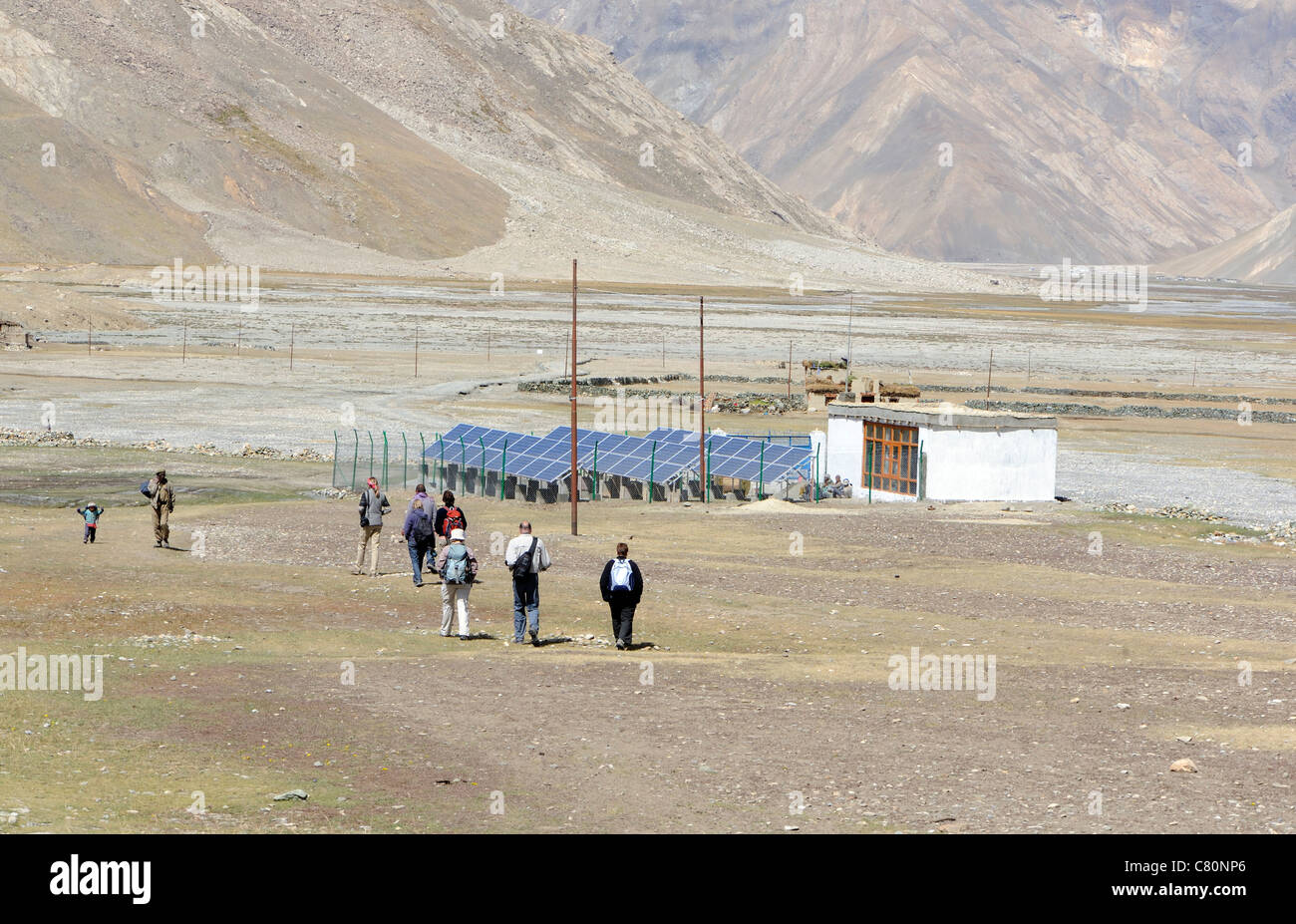 A group of tourists walk past a government built solar panel farm in the village of Rangdum in Zanscar. Rangdum, Zanscar, Ladakh. India Stock Photo