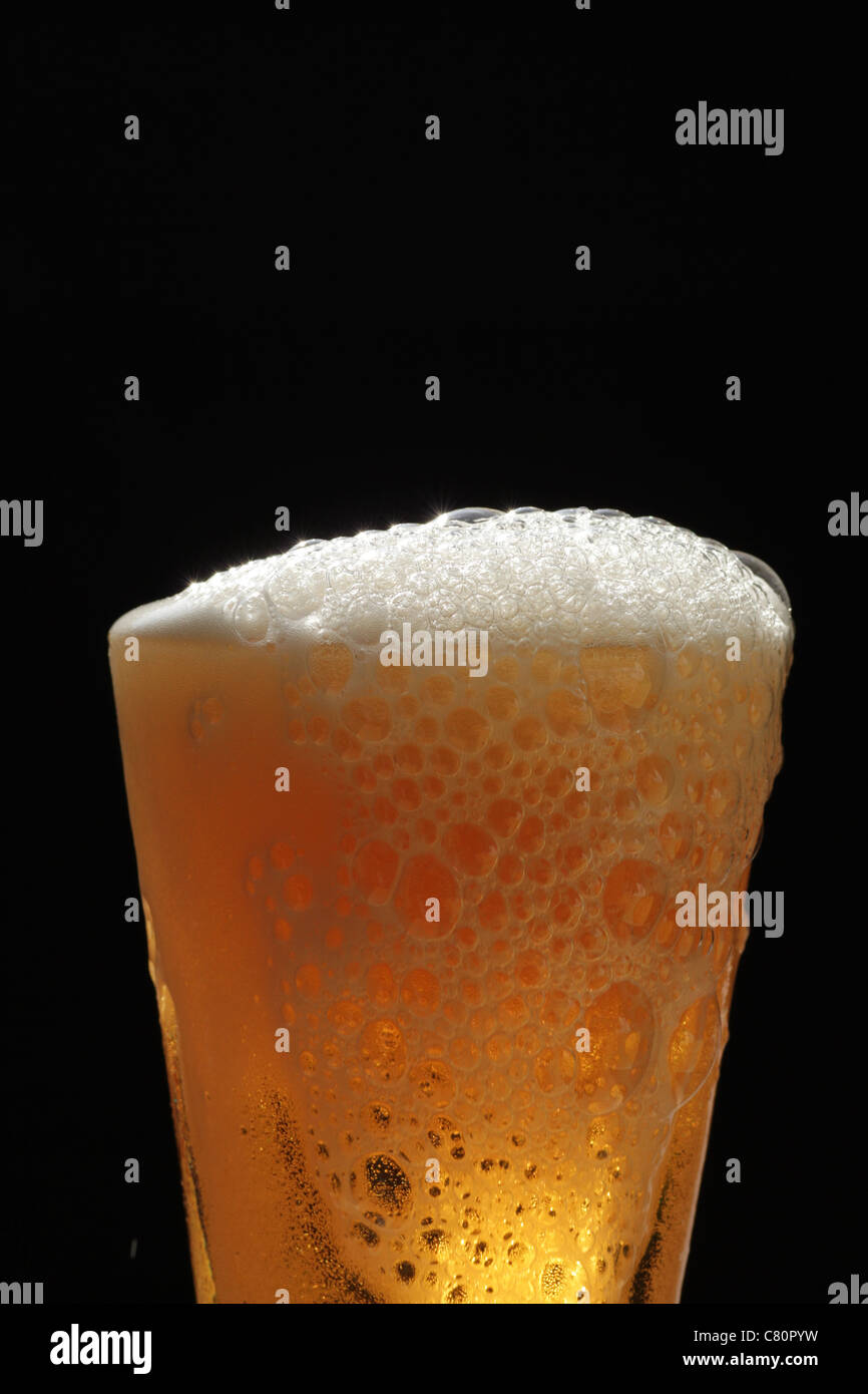 Head of beer froth Close up of beer being poured into glass running froth over top of glass good head on beer black backdrop Stock Photo
