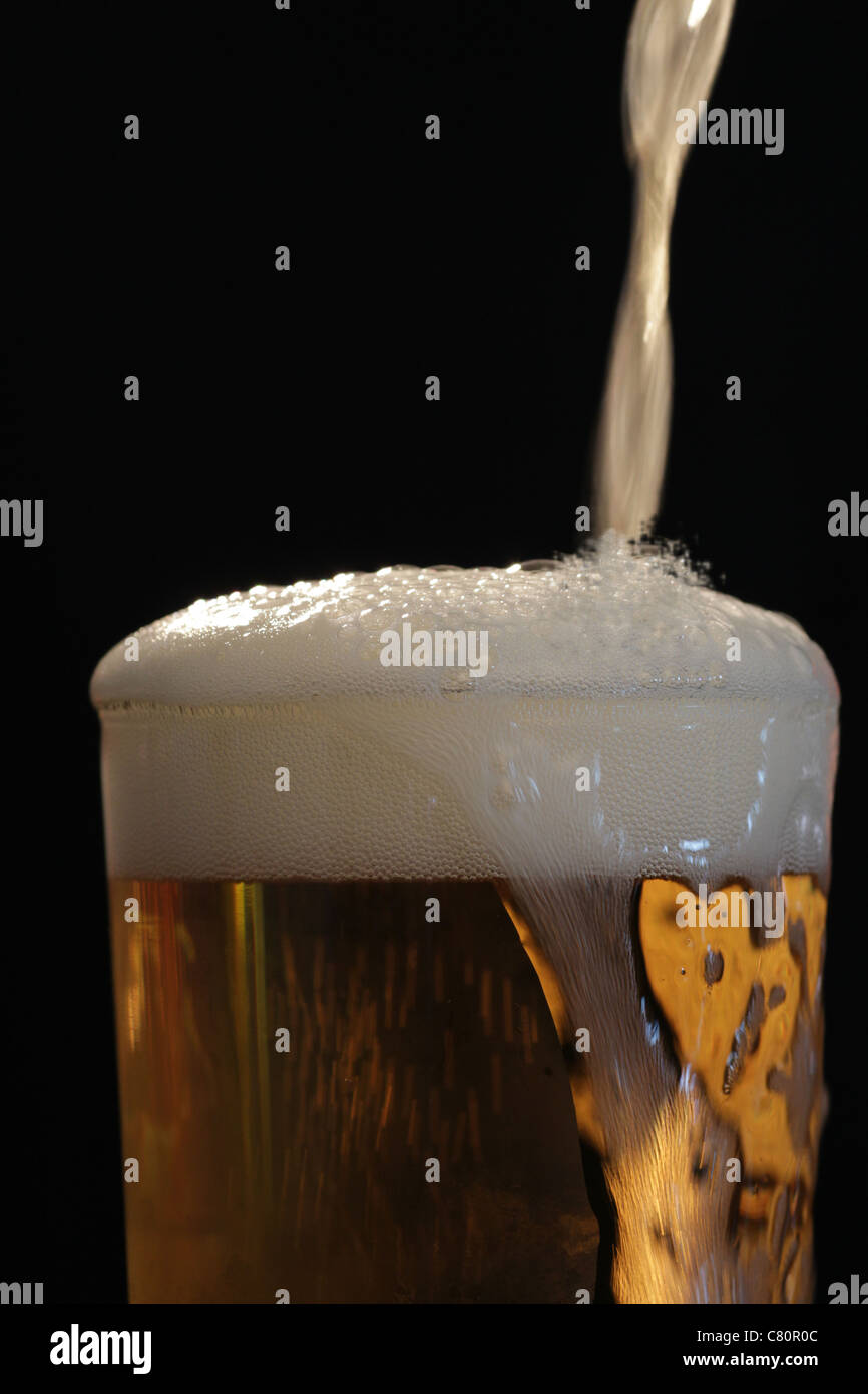 Head of Beer Close up of beer being poured into glass  good head on beer black backdrop Stock Photo