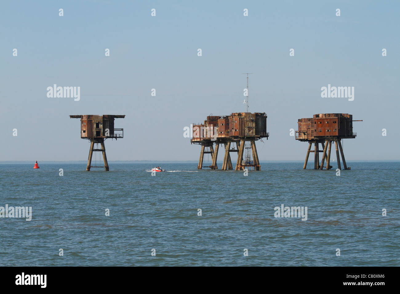 The abandoned wartime Red Sands fort in the Thames estuary. A boat passes in front of them. Stock Photo