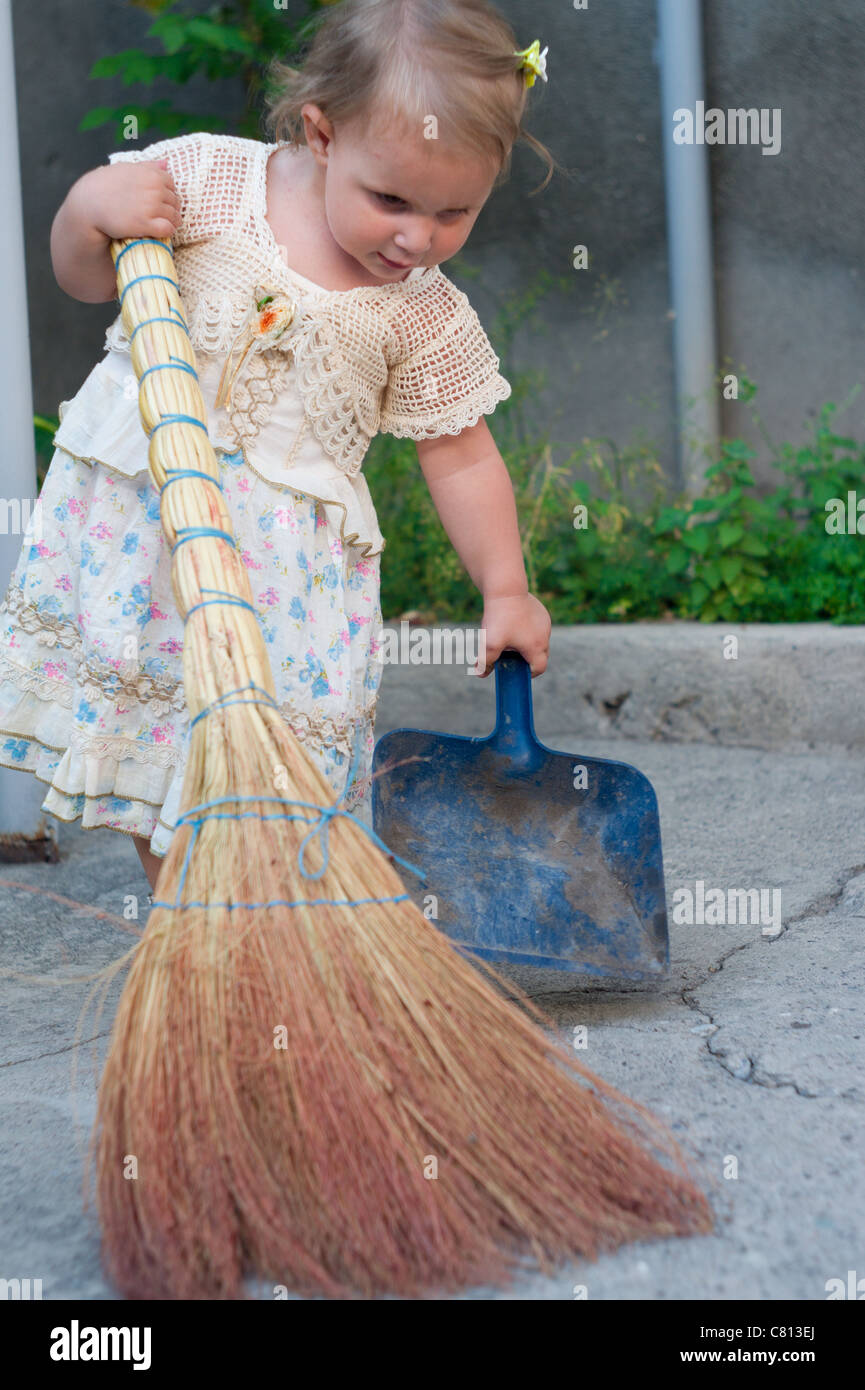 An innocent baby girl doing her first steps in sweeping the yard Stock Photo