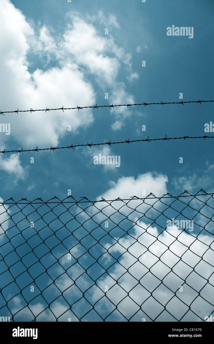 Barbed wire fence against a blue sky with clouds Stock Photo - Alamy