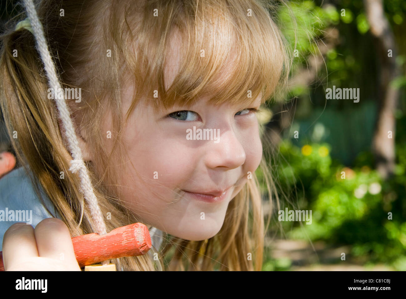 Cheerful little girl shakes on a swing Stock Photo