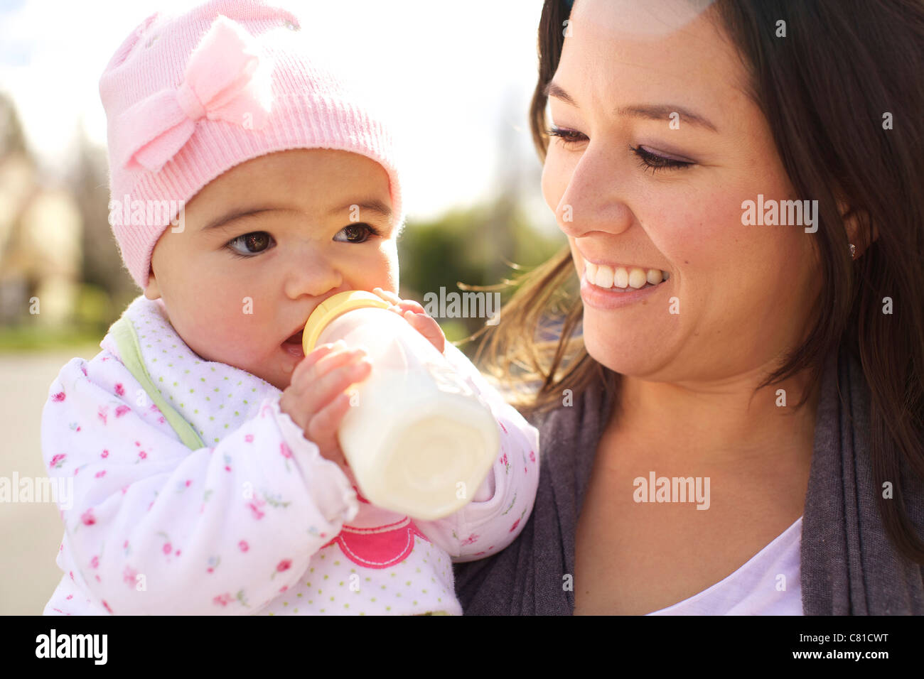 Mixed race mother watching baby girl drinking bottle Stock Photo