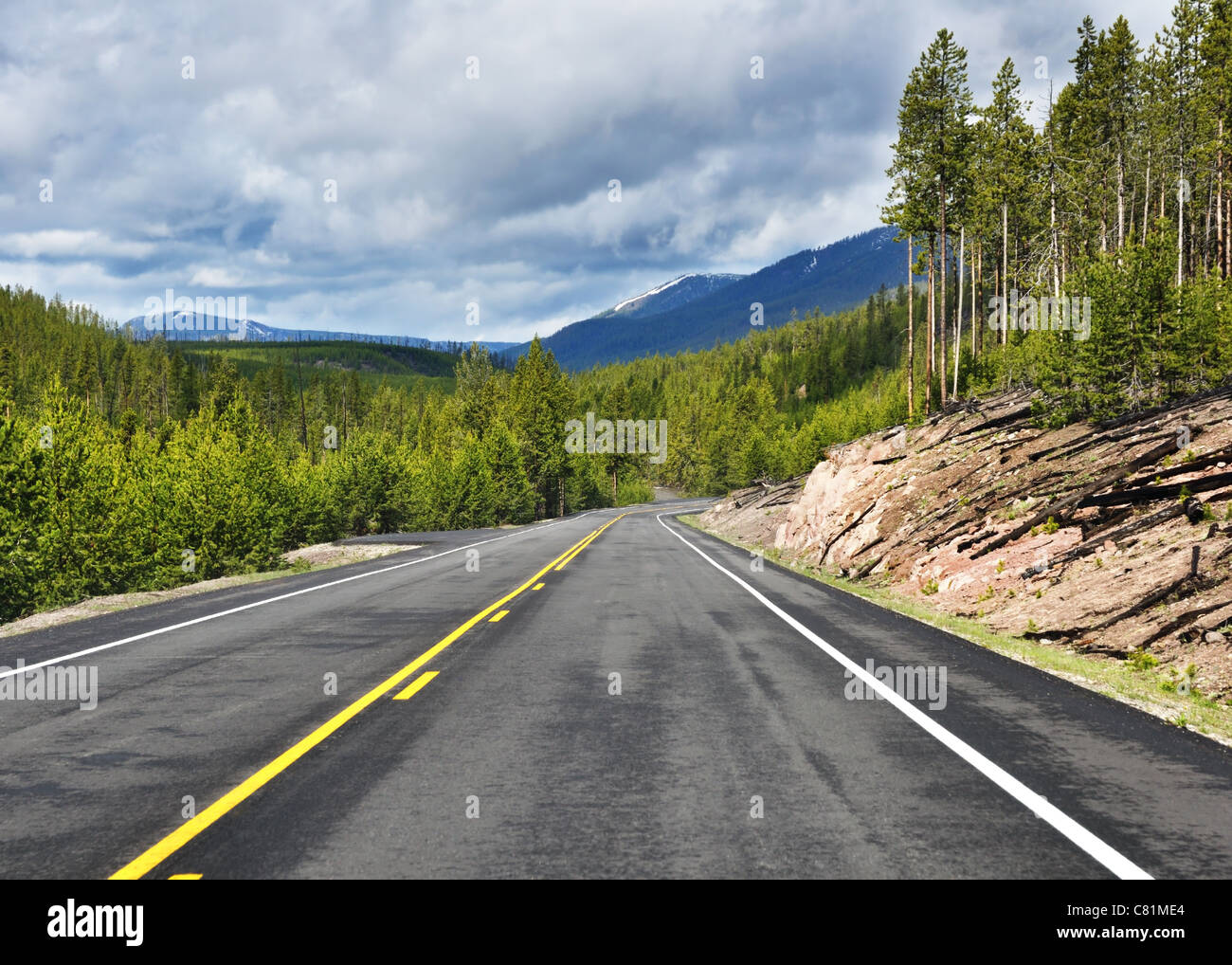 Asphalt road in mountains with forest and cloudy sky Stock Photo - Alamy